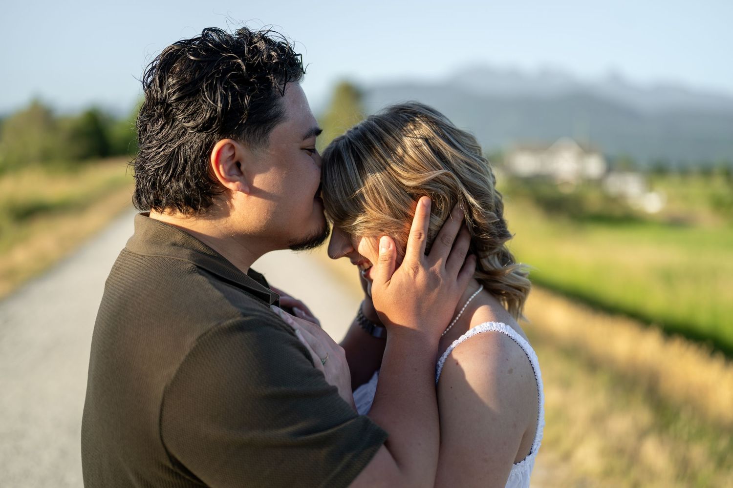 Romantic couple sharing a tender kiss outdoors on a sunny day with mountains in the background.