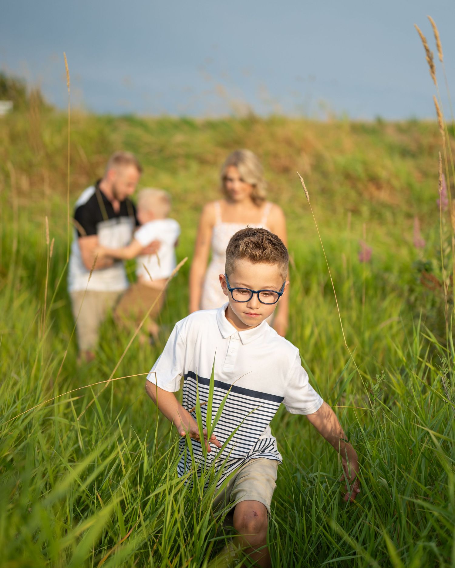 Child playing in tall grass field during summer photoshoot.