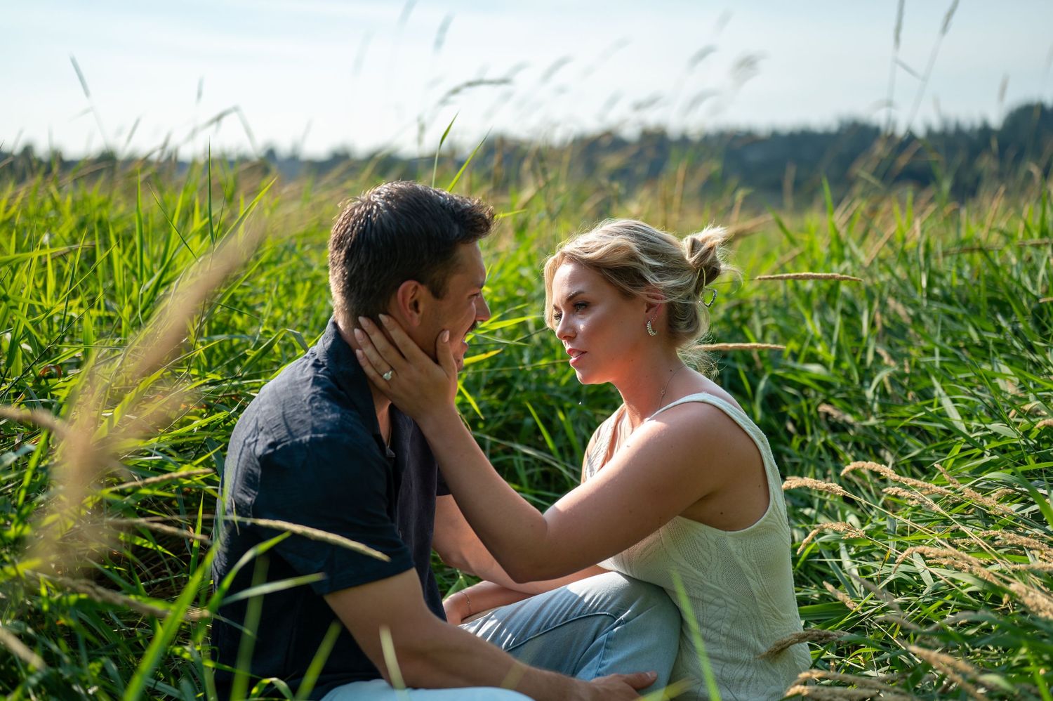 Two people share intimate moments in a field of tall grass during golden hour.