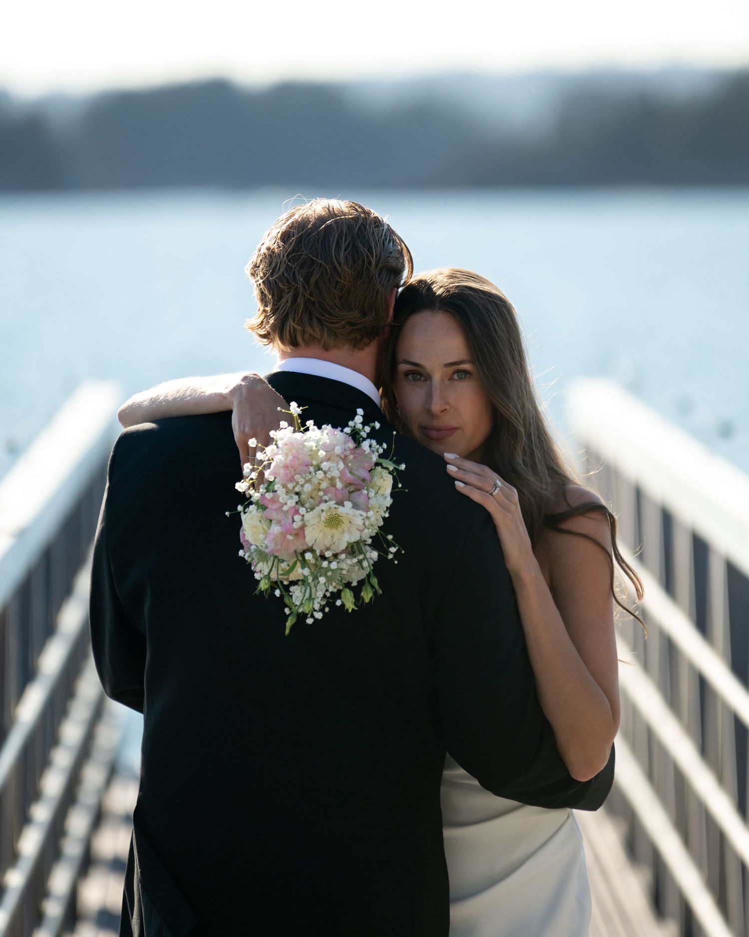 Newlyweds share romantic moments on wooden dock overlooking tranquil waters.