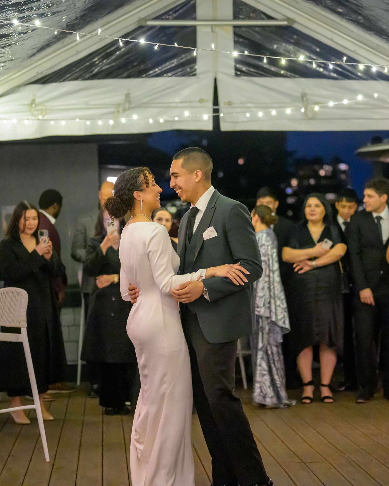 Wedding guests dancing together under string lights at outdoor reception.