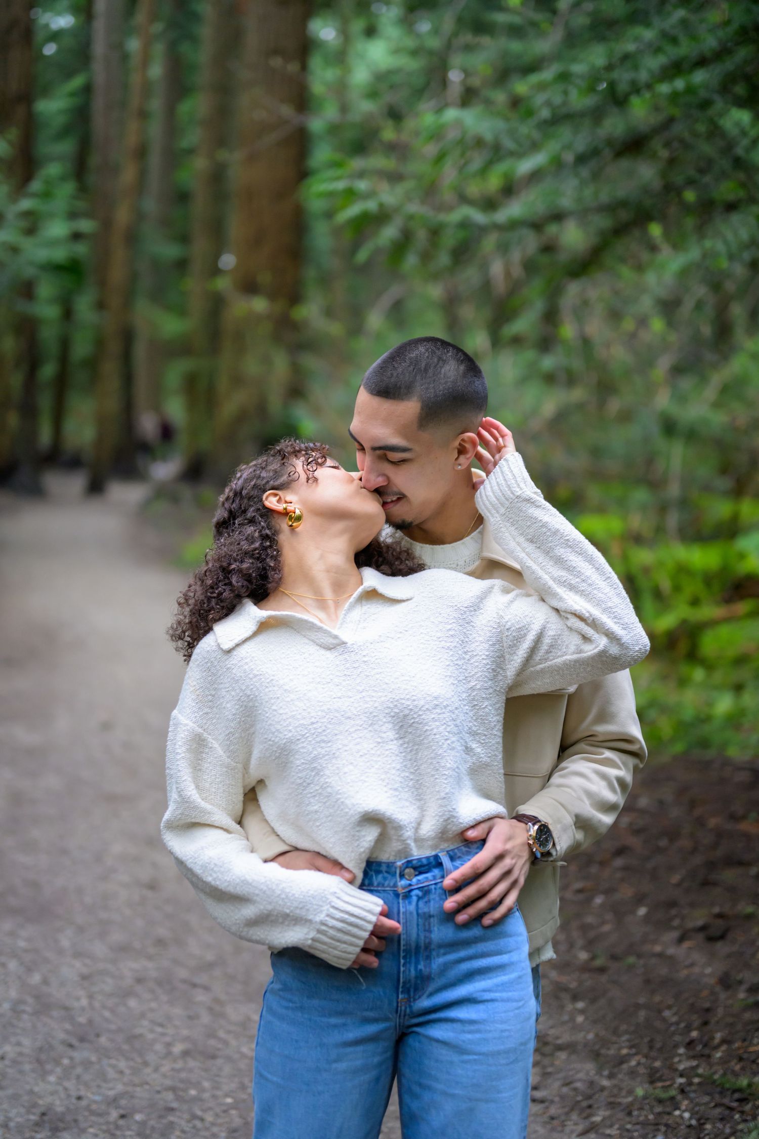 Couple in casual outfits sharing tender moments on a forest path.