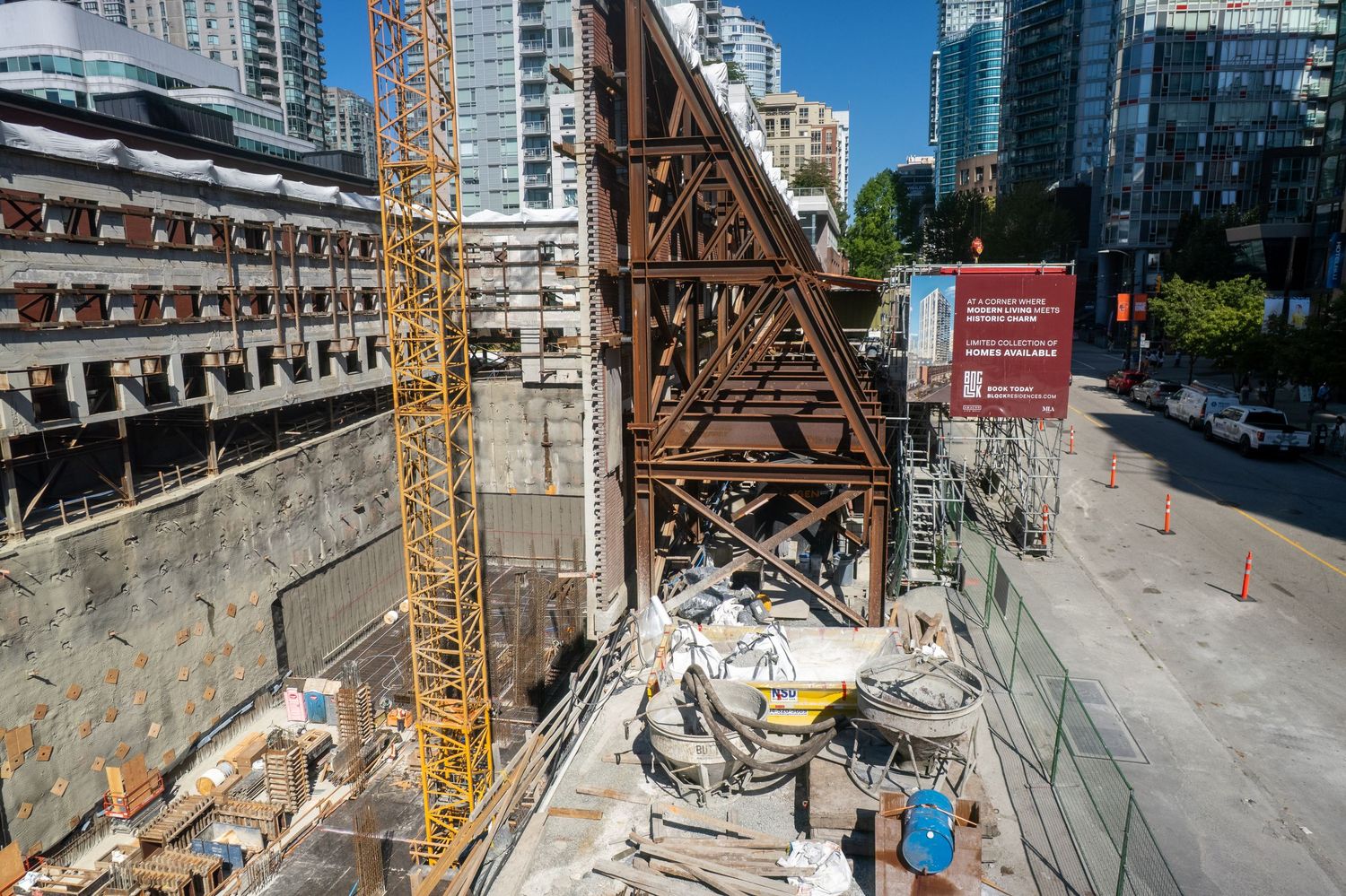 Construction site panorama showing tall buildings and cranes against blue sky in urban setting.