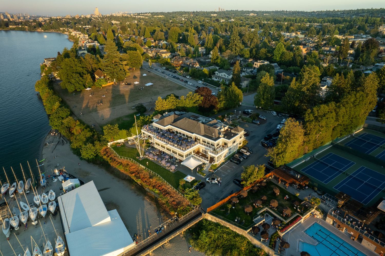 Aerial view of waterfront property with tennis courts and marina surrounded by trees.