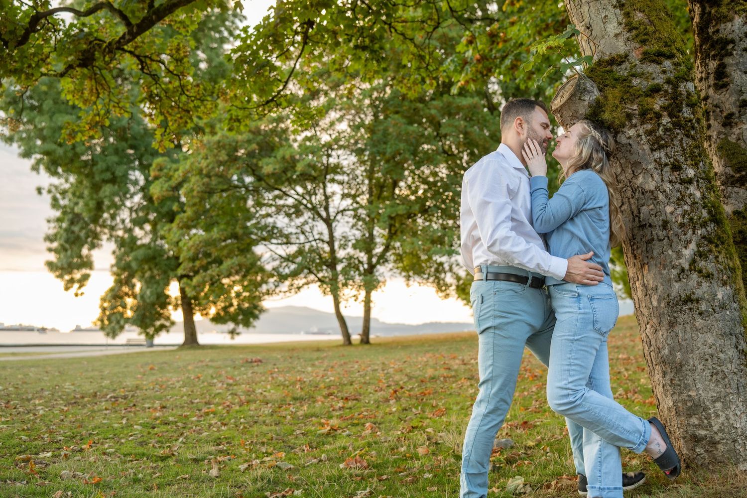 Couple sharing a romantic moment leaning against a tree in a lush autumn park at sunset.