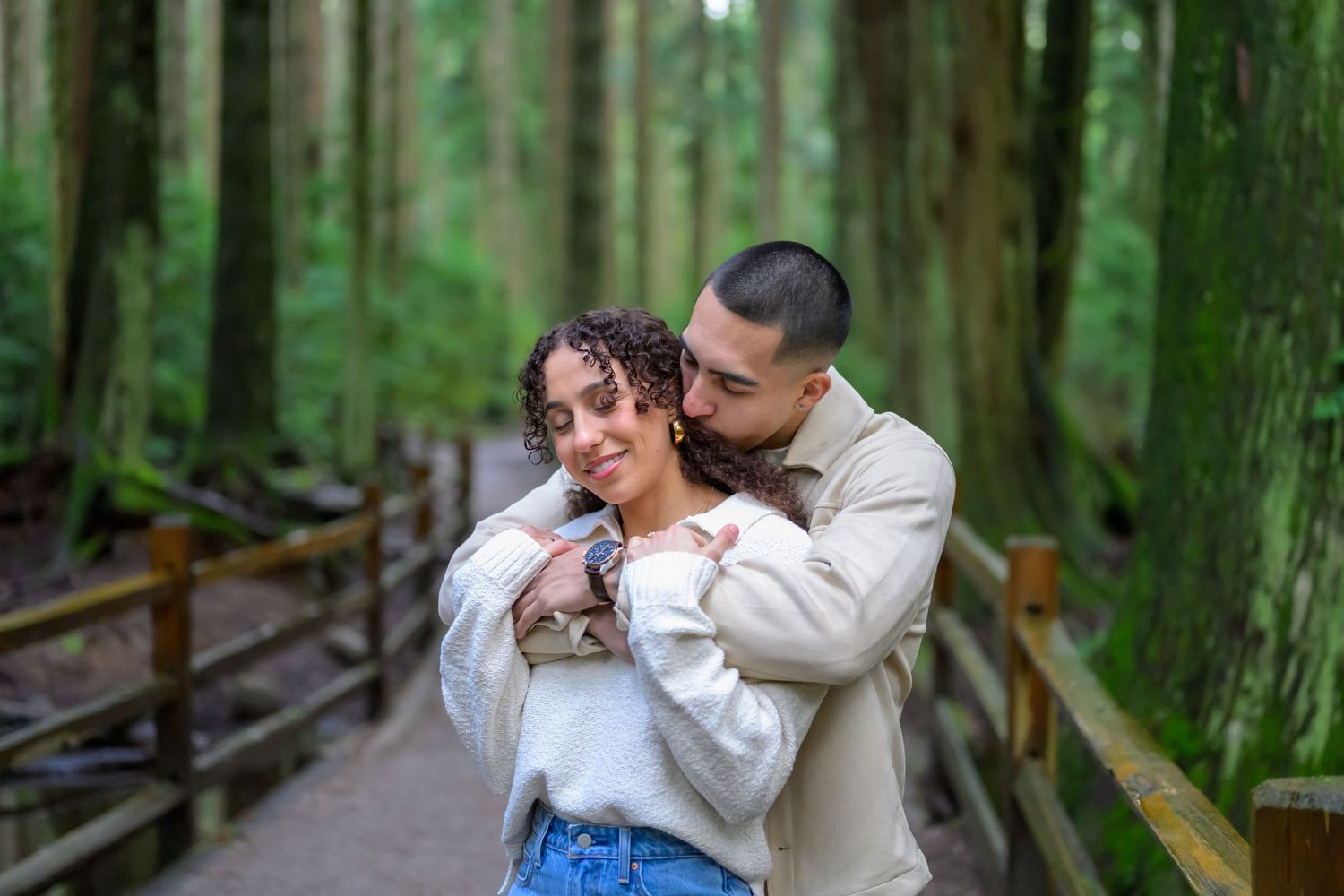 Couple embracing on a wooden boardwalk surrounded by lush green forest.