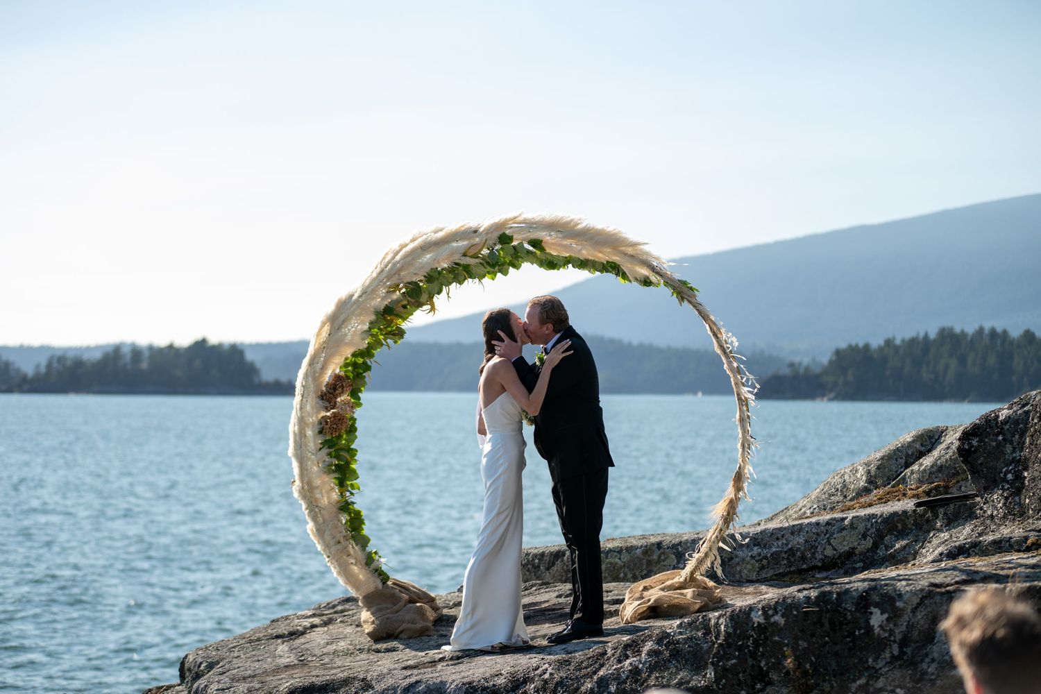 Wedding ceremony under floral arch on dramatic rocky coastline with ocean views.