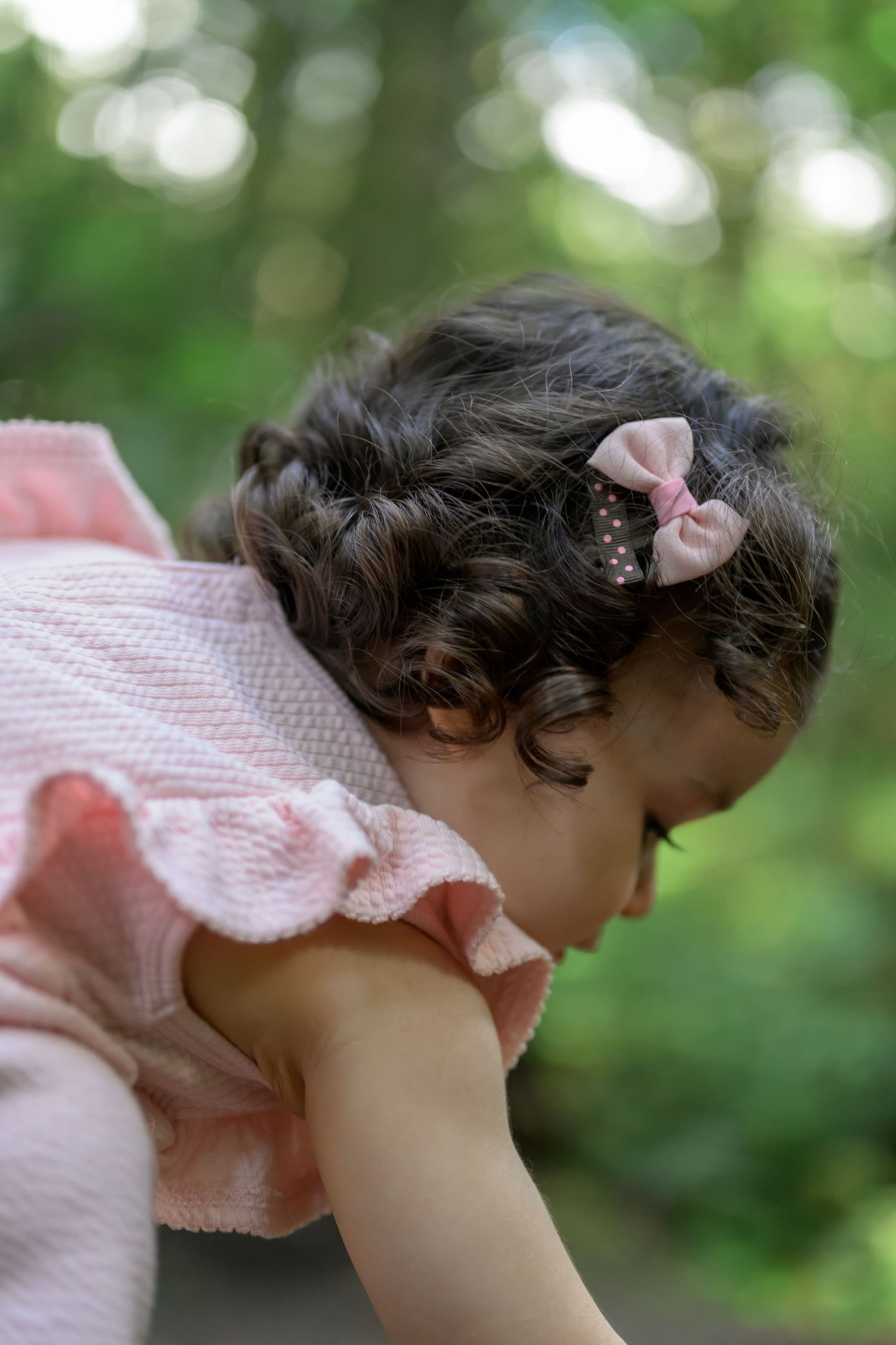 Close-up profile view of small child in pink ruffled dress against blurred green background.