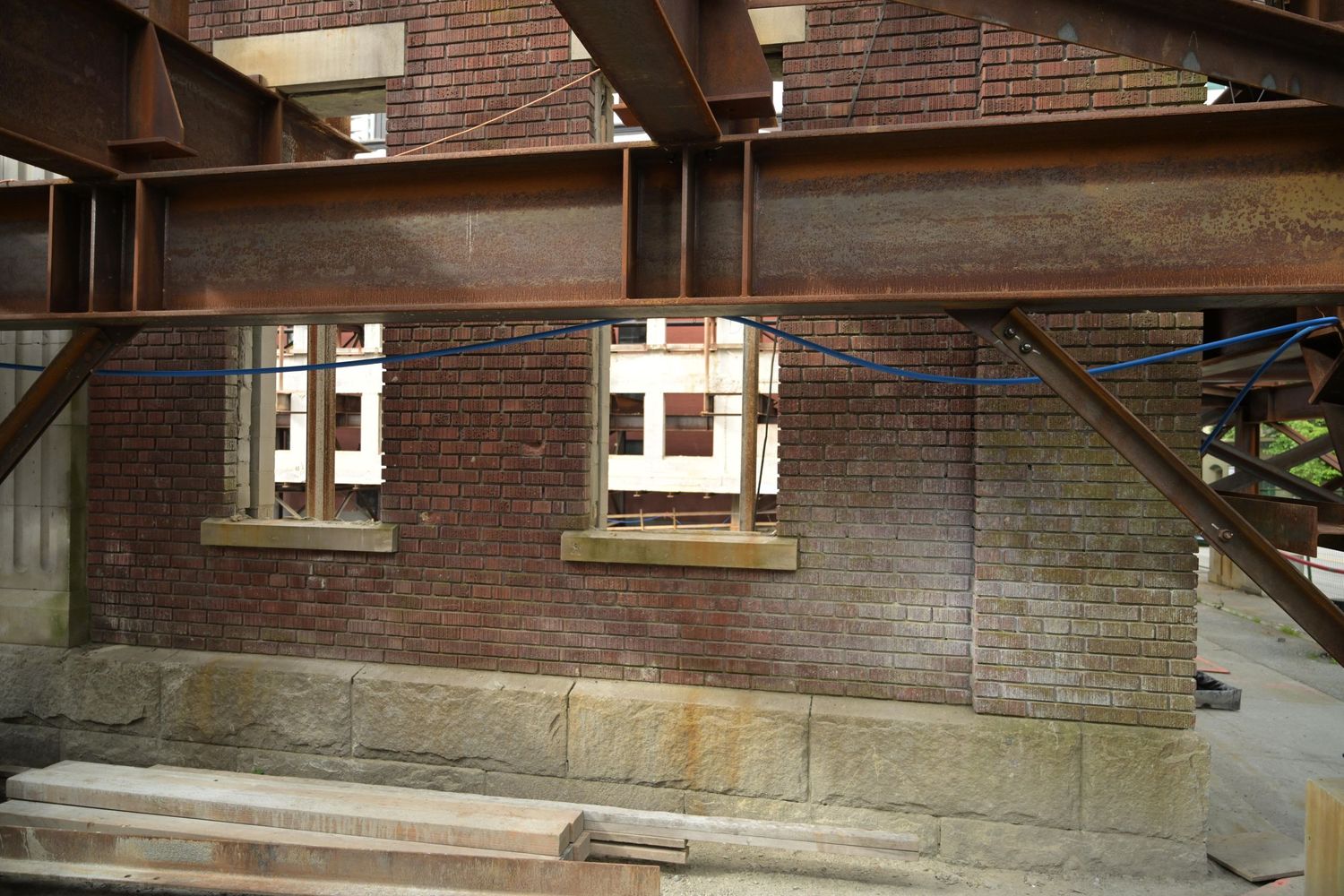 Brick building exterior with two small windows and exposed steel beams during renovation.