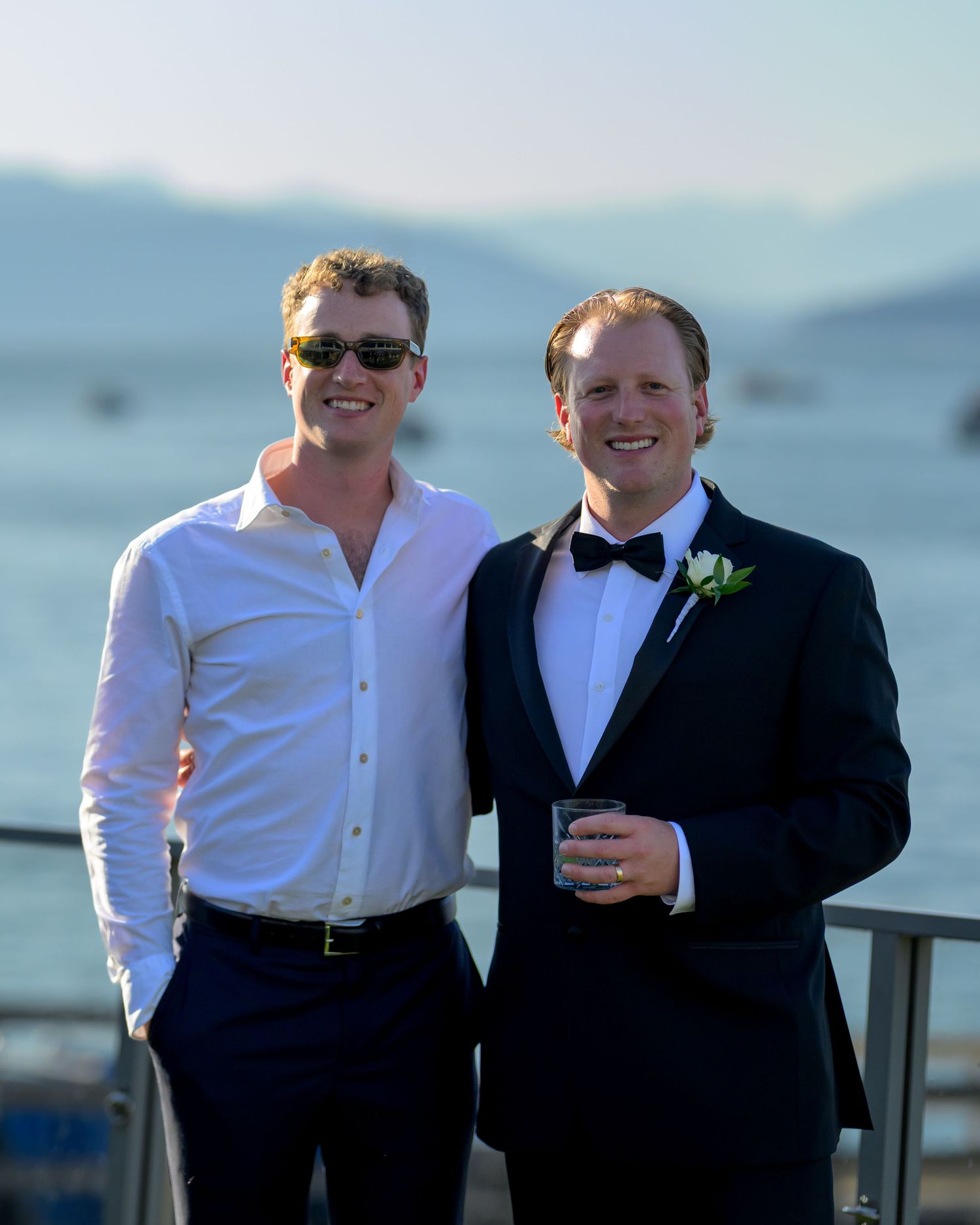 Groomsmen in formal attire pose together on waterfront deck.