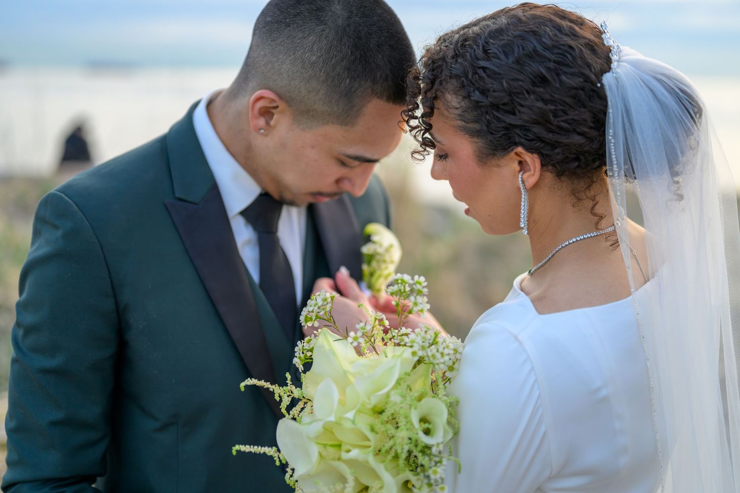 Elegant wedding couple sharing intimate moment with green floral bouquet.