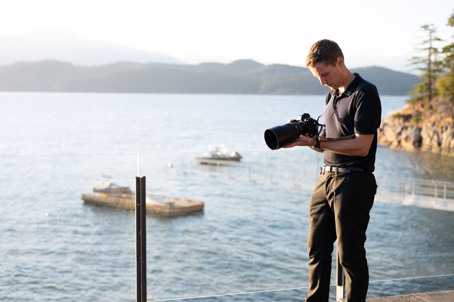 A photographer capturing scenic shots along a rocky coastline with boats in the distance.
