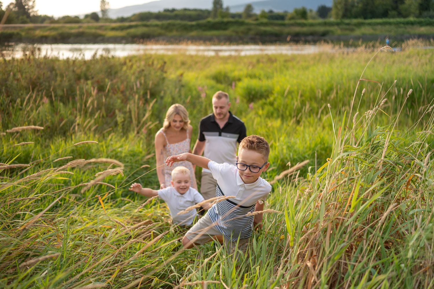 A family sits together in tall grass near a wetland during golden hour as sunlight illuminates the natural landscape. Pitt Meadows beach.