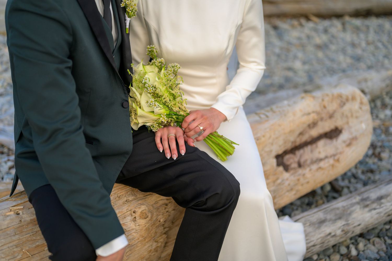 Wedding bouquet of white and green flowers held between bride in white dress and groom in dark suit.