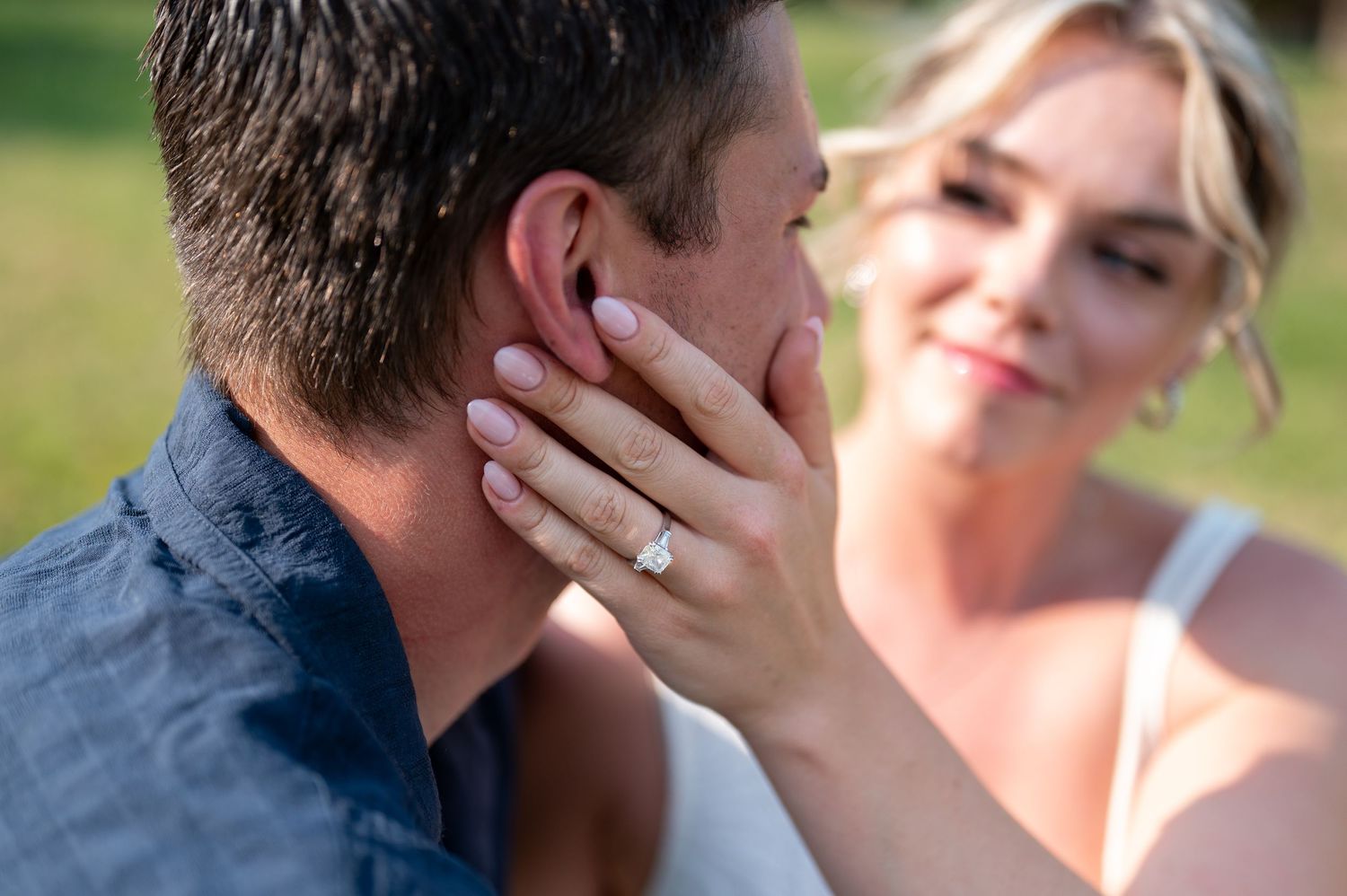 Woman showing off engagement ring while tenderly touching man's face outdoors.