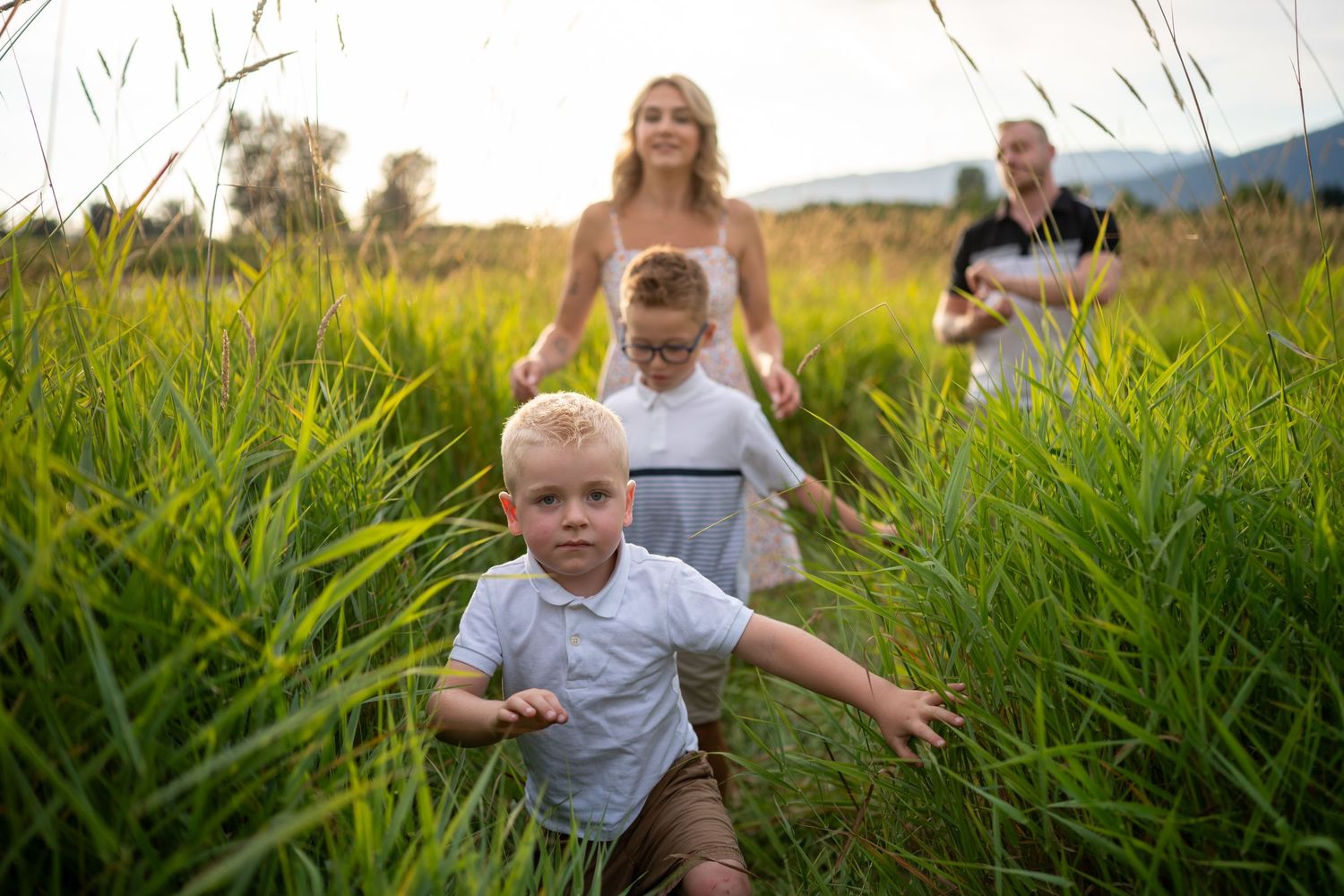 Candid family moments captured in golden hour light among tall grass.