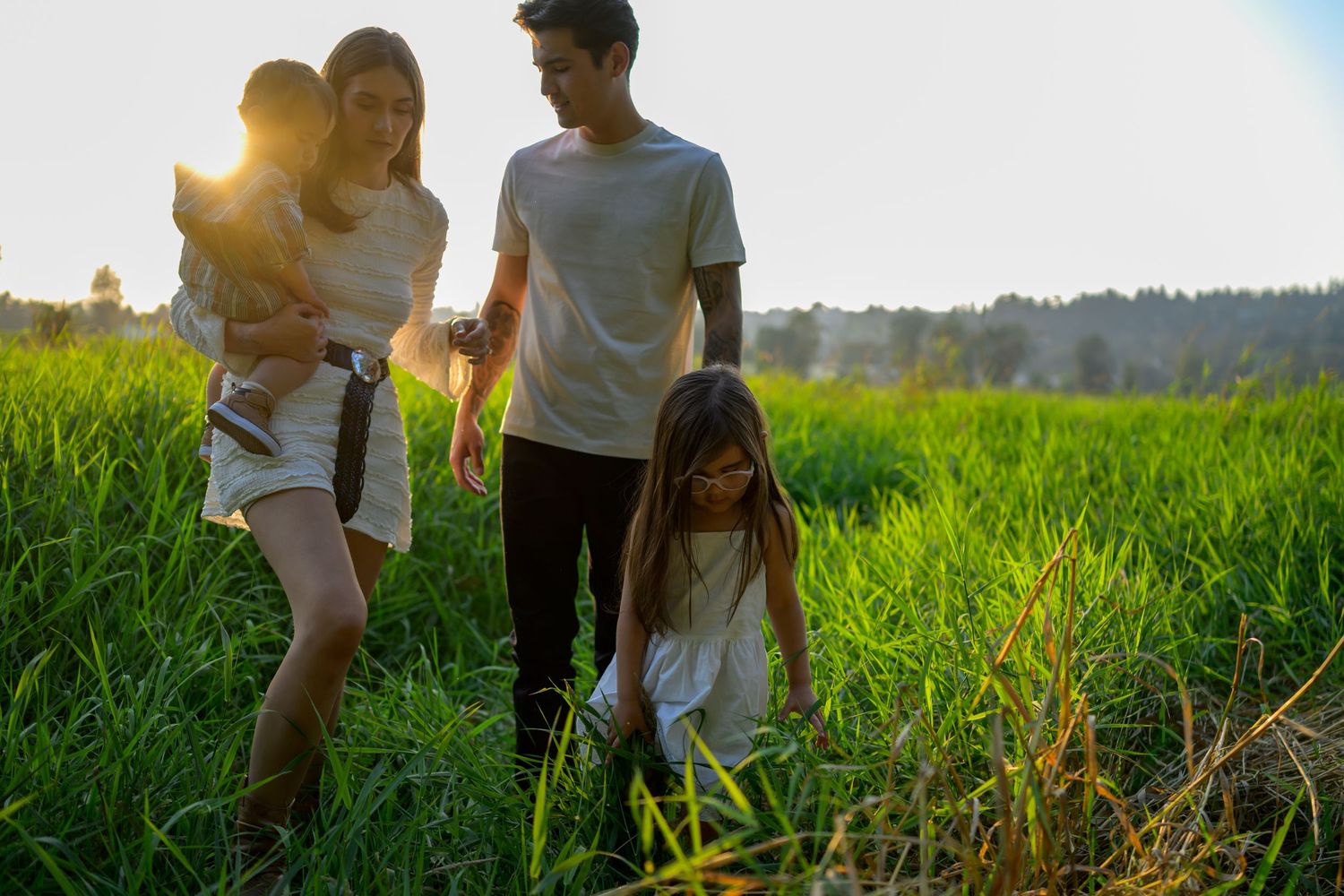 Group walking through a sunlit grassy field with mountains in background.