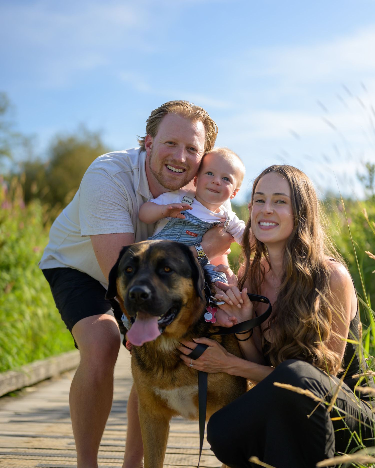 Family photoshoot with German Shepherd dog on wooden boardwalk during sunset.