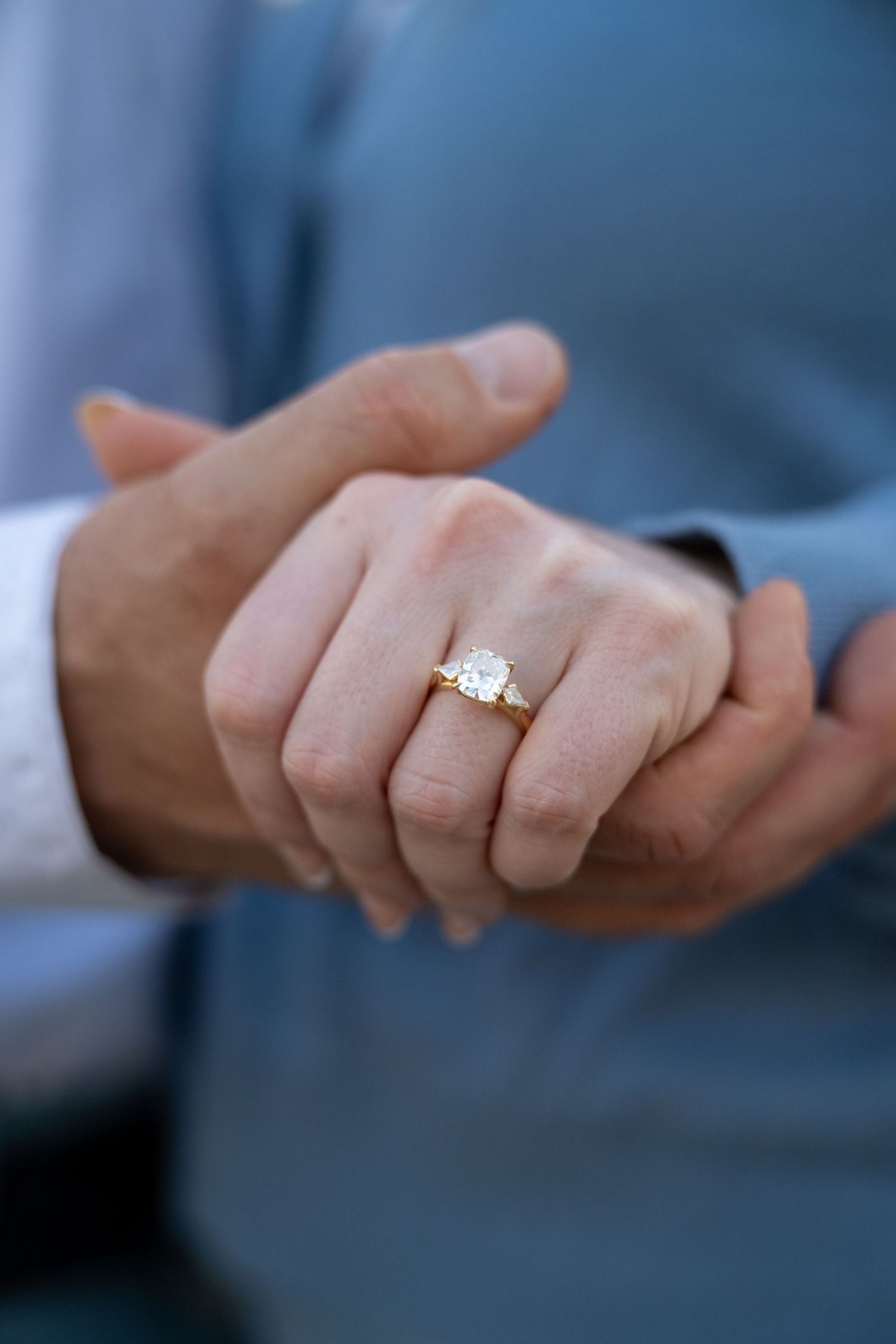 Close-up of two hands holding, featuring a gold diamond engagement ring on a woman's finger.