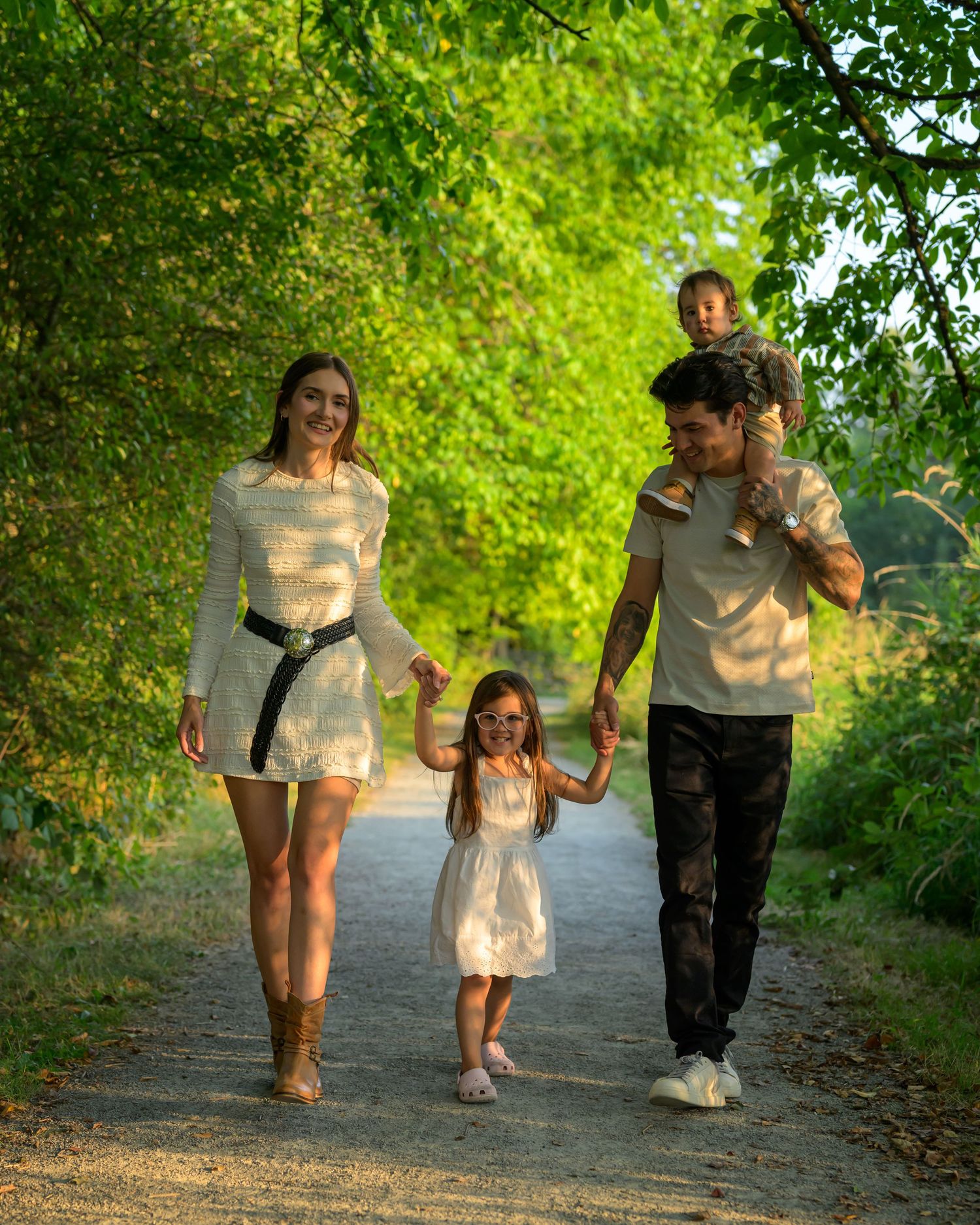 Family walking together on a tree-lined path during golden hour sunset.