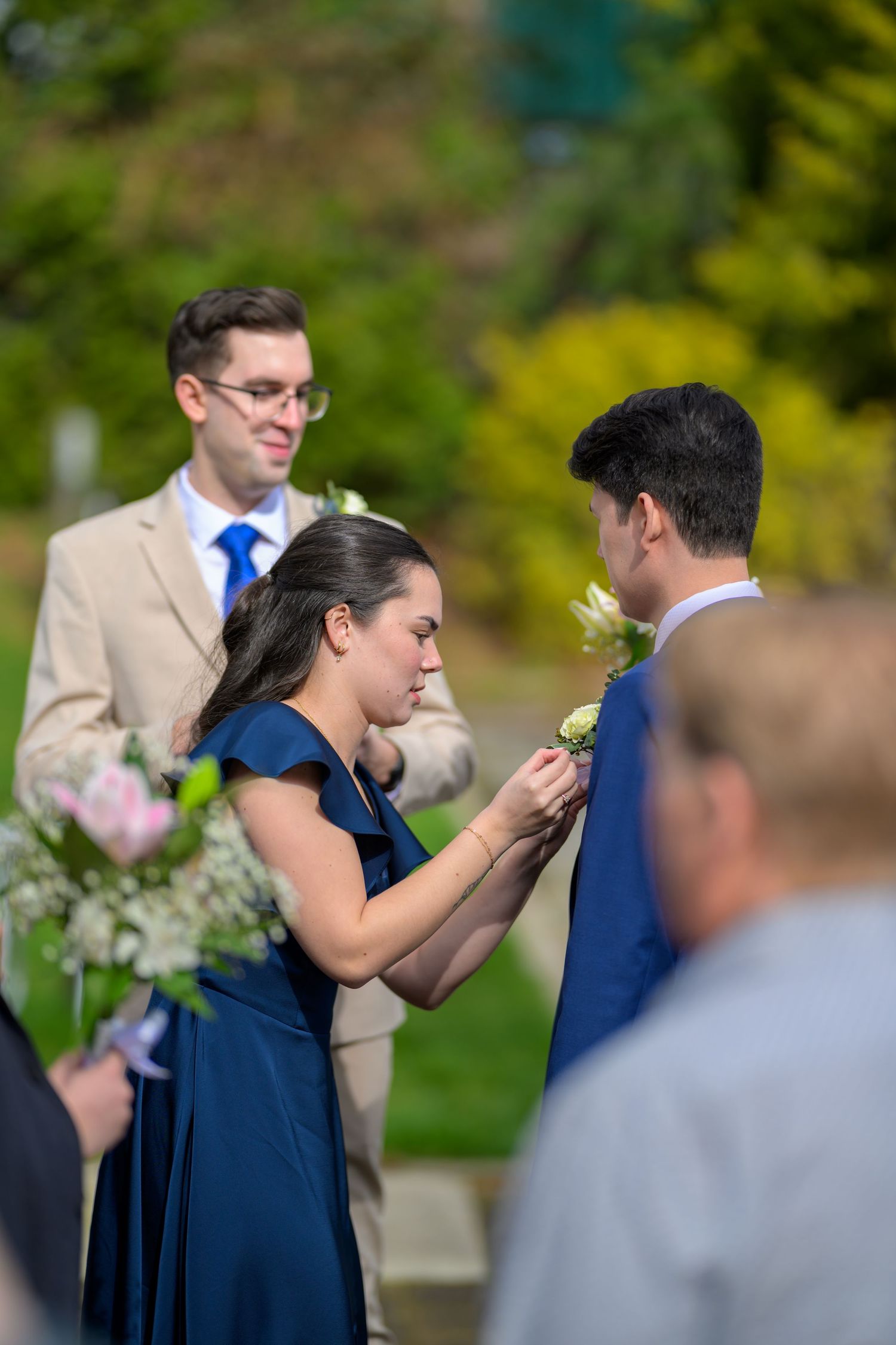 Wedding guests in formal attire gather during outdoor garden ceremony.
