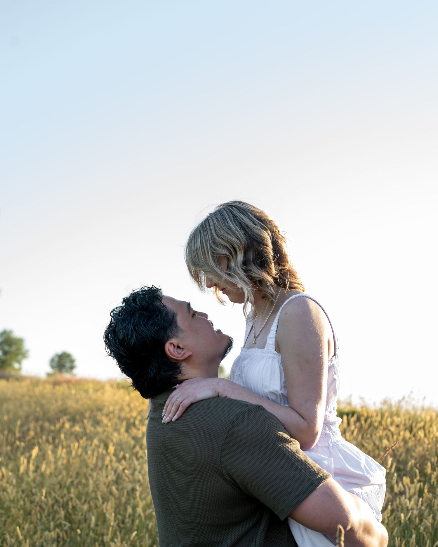 A couple shares a romantic moment in a golden wheat field, as a man lifts a woman in a white dress toward a kiss.