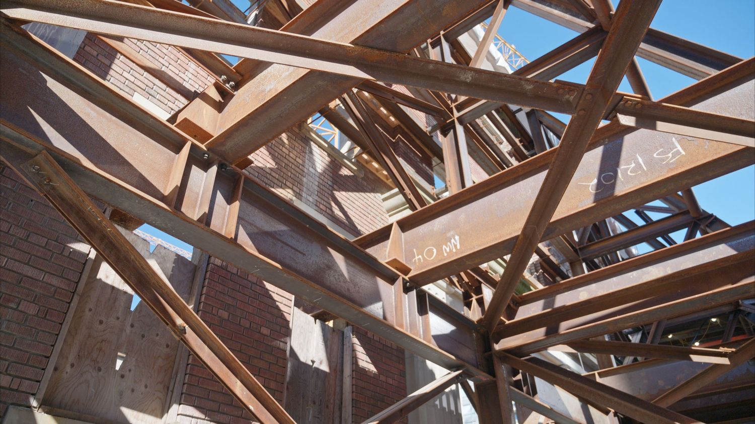 Wooden roof trusses and beams under construction with blue sky visible through framework.