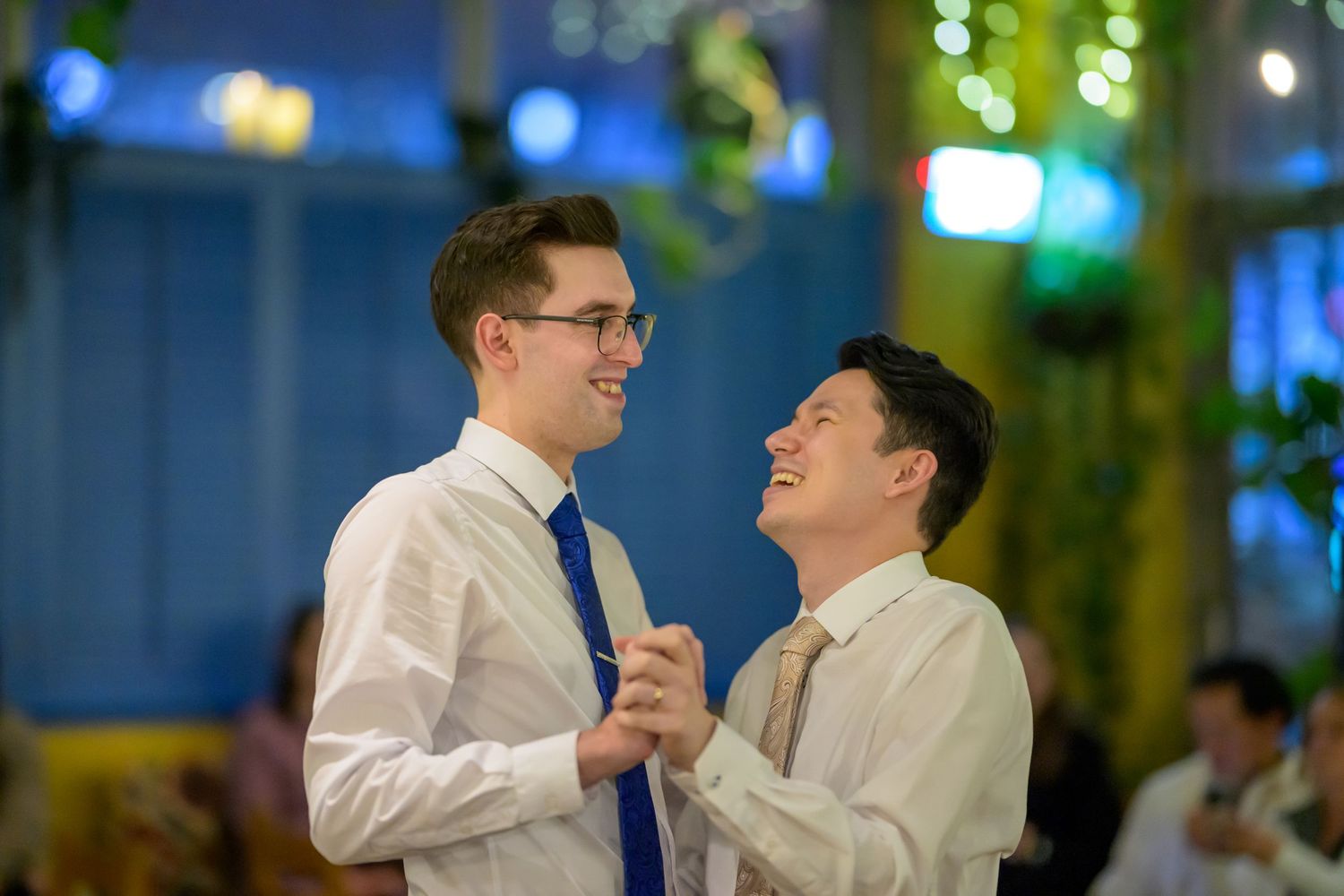 A couple shares a romantic dance together at an indoor wedding reception with green lighting in the background.