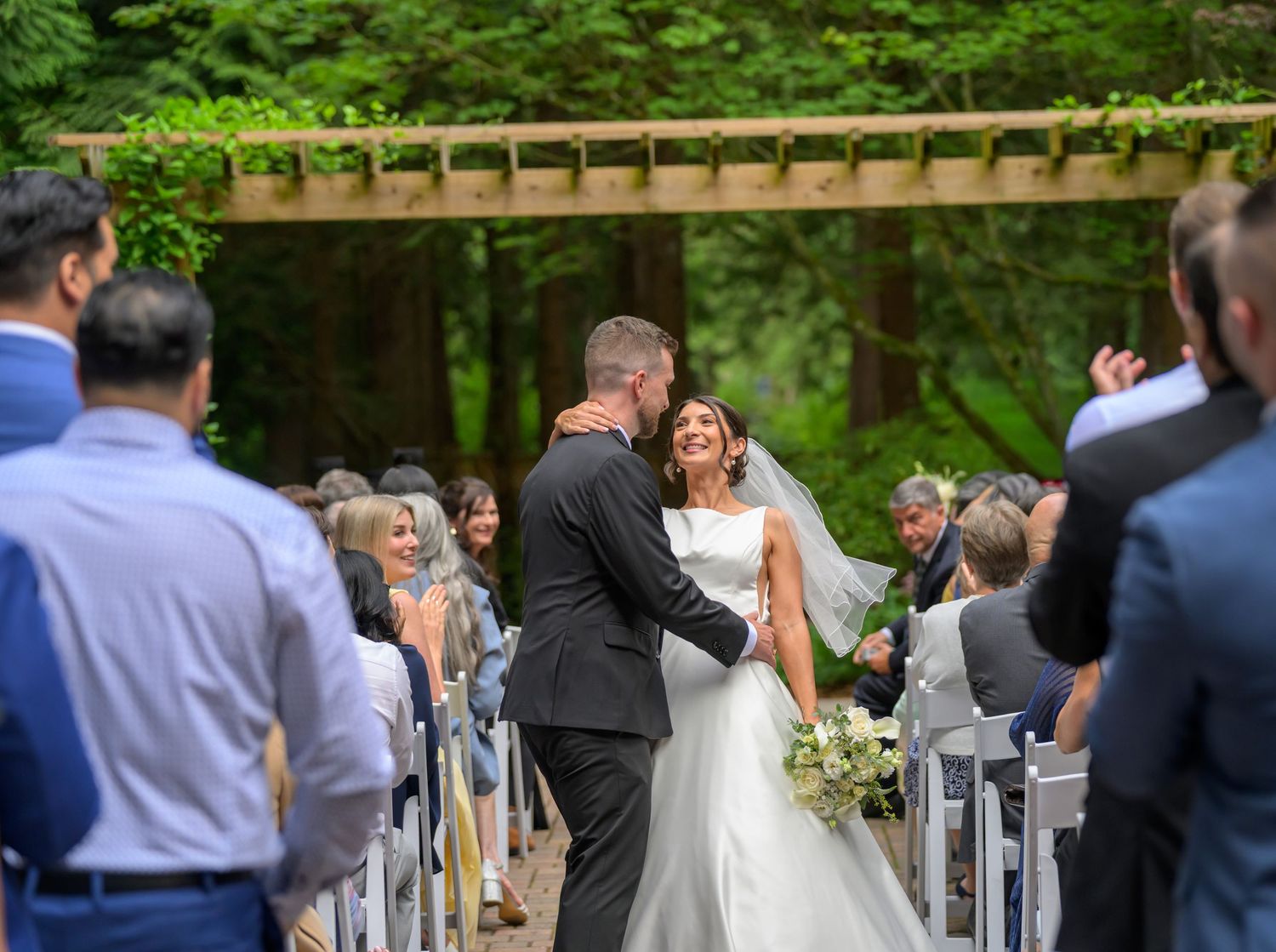Bride and groom share a joyful moment walking down the aisle at an outdoor forest wedding ceremony.