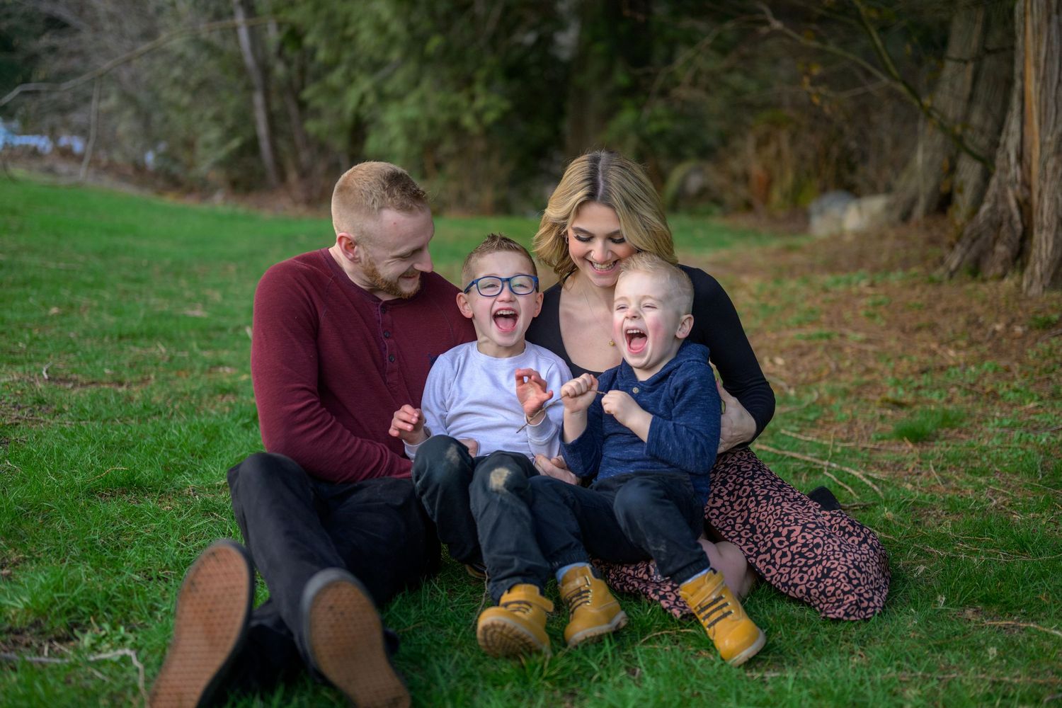 A family shares laughs together during an outdoor photo session in a green park setting.