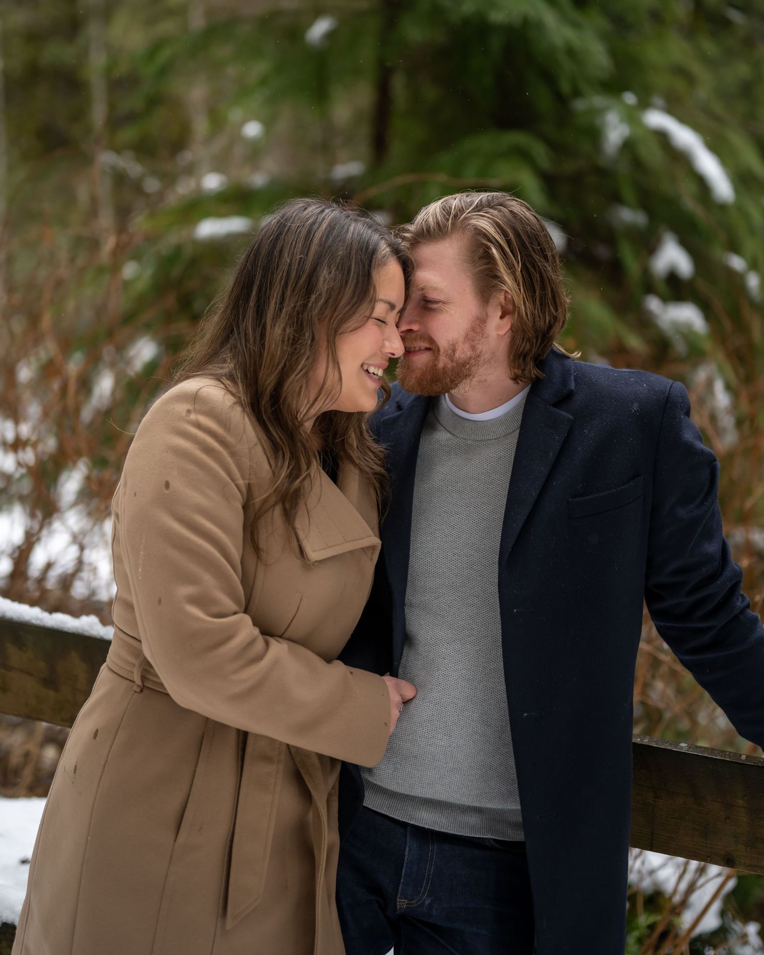 Romantic winter photoshoot with couple in coats among snow-covered trees.