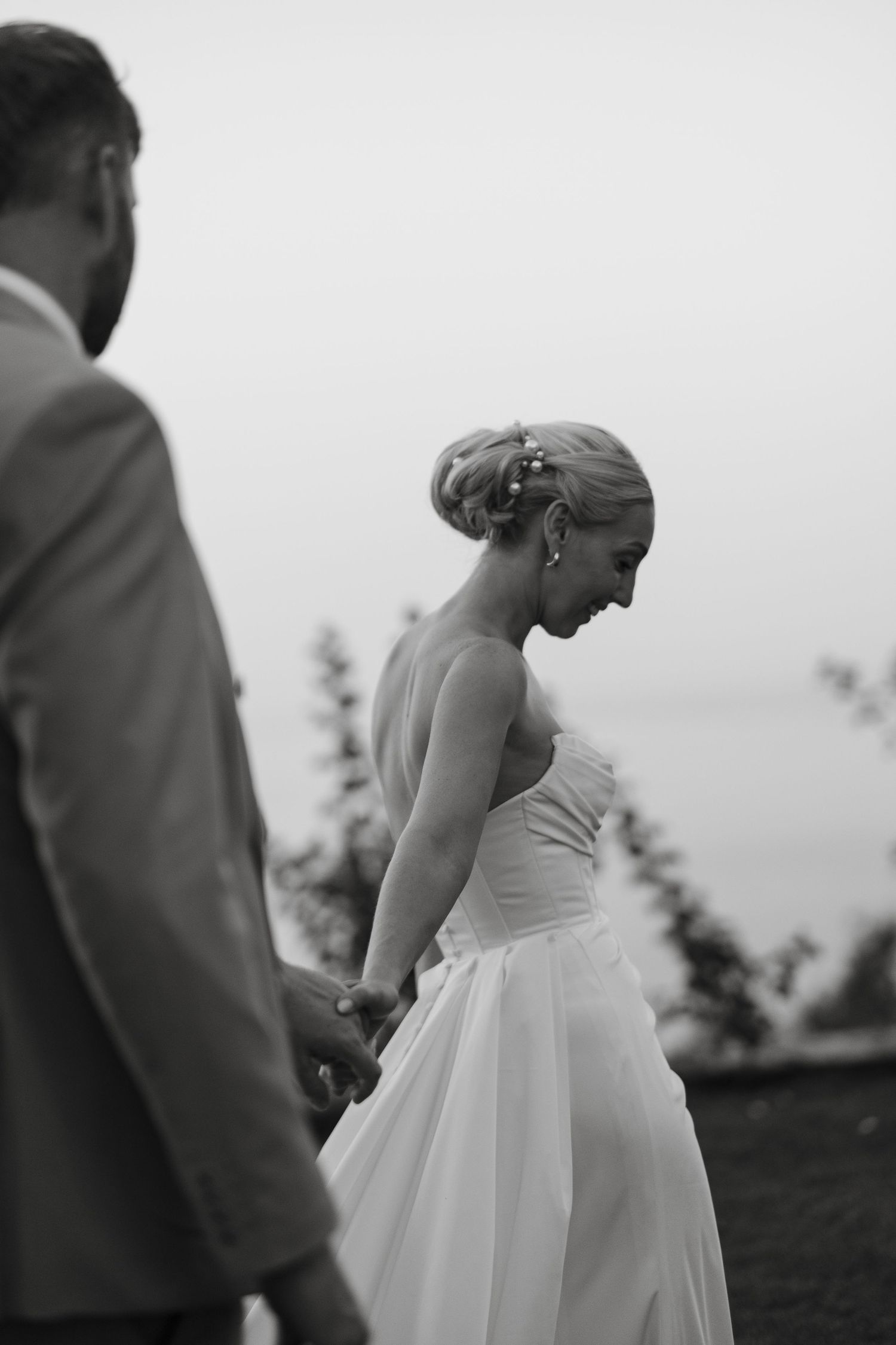 Black and white photo of bride and groom holding hands walking outdoors at dusk.