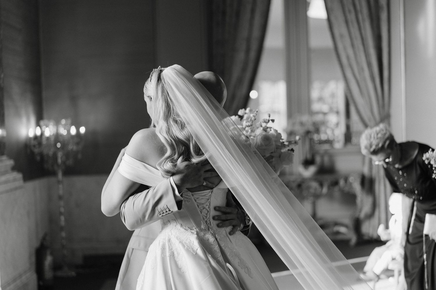 Black and white photo of bride in gown and veil holding bouquet indoors.