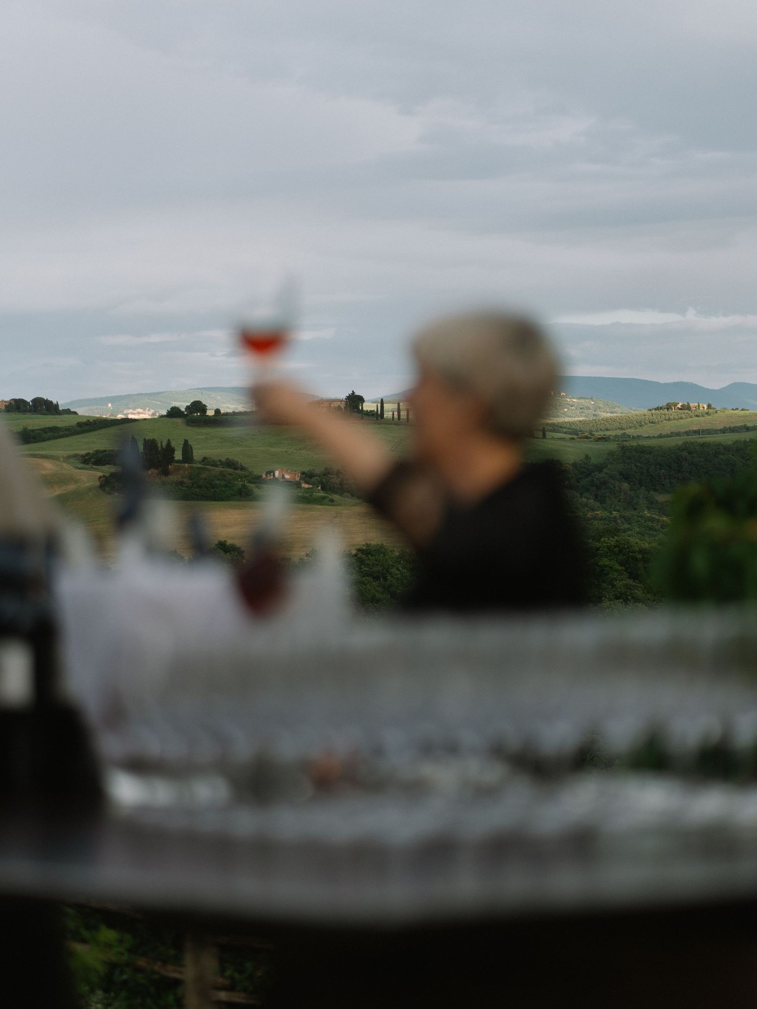 Guest raises a glass of rose wine with rolling Tuscan hills in the background at sunset.