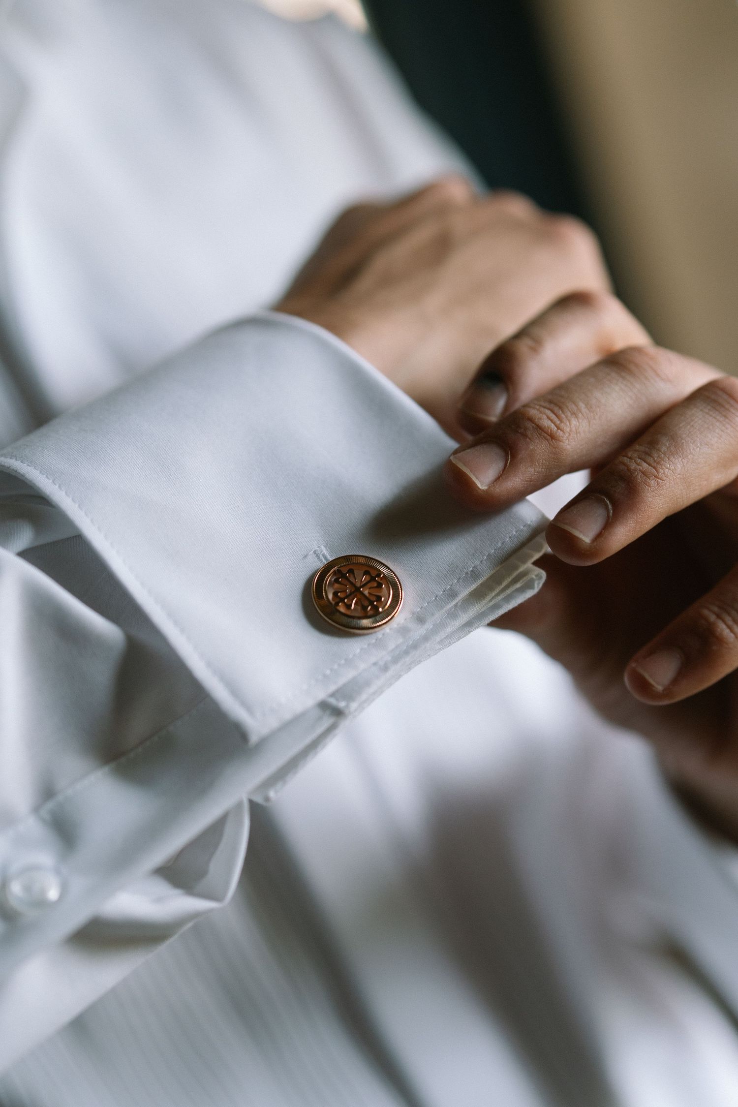 Groom fastening an ornate gold cufflink on a white dress shirt sleeve before the wedding.