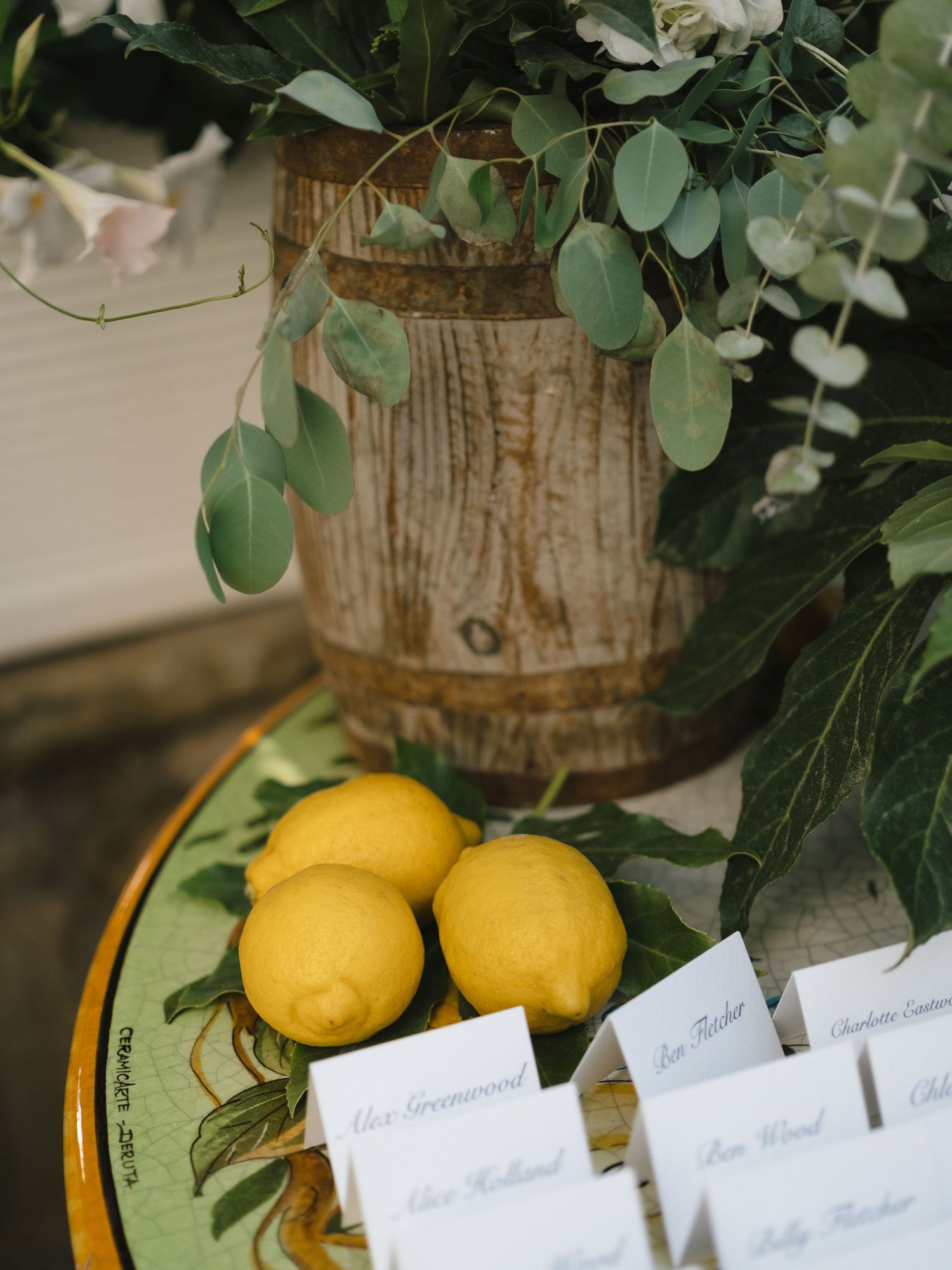 Wedding escort cards displayed beside fresh lemons on a decorative plate with greenery centerpiece.