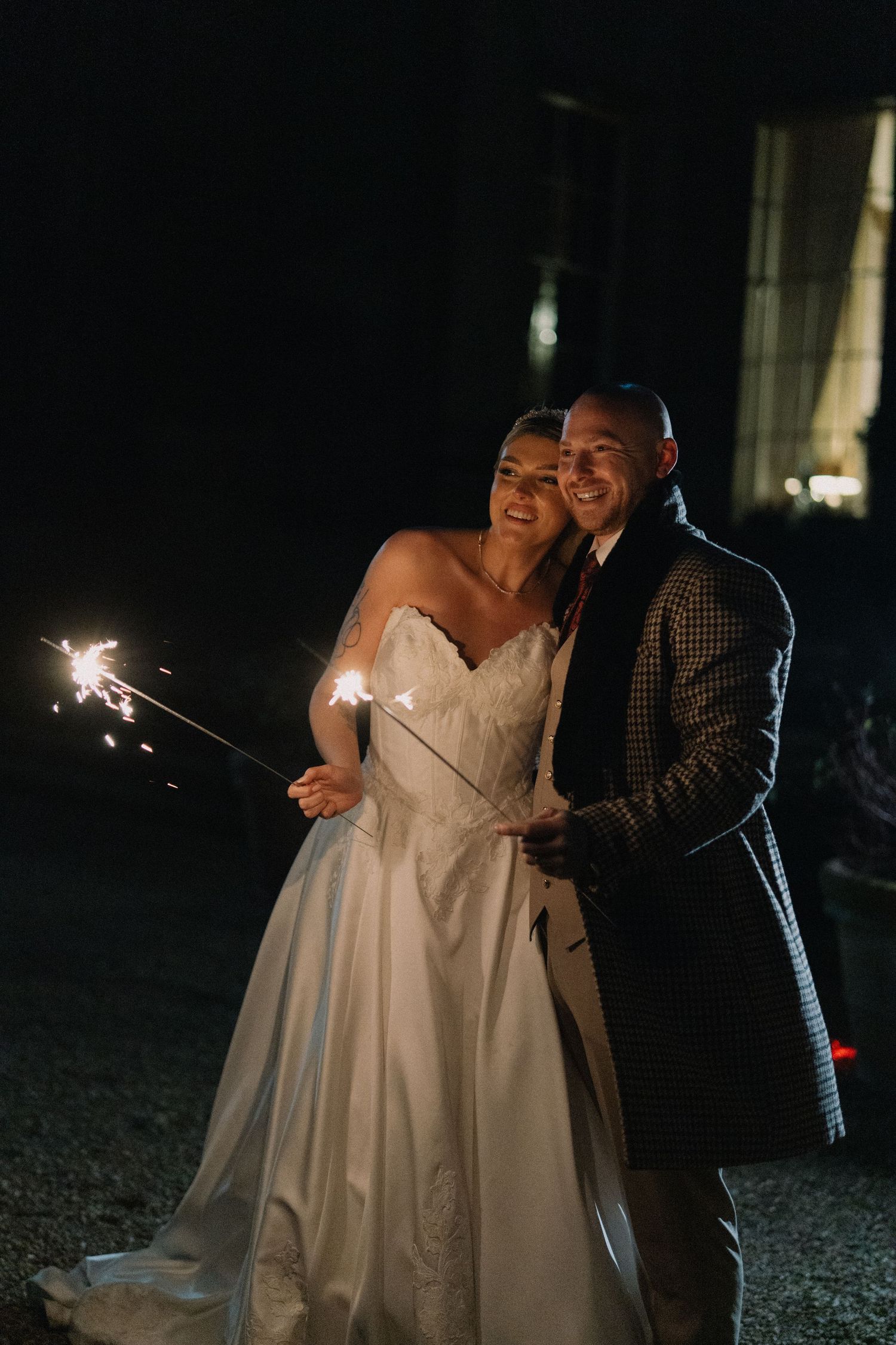 Bride and groom holding sparklers together at night, smiling during their wedding celebration outdoors.