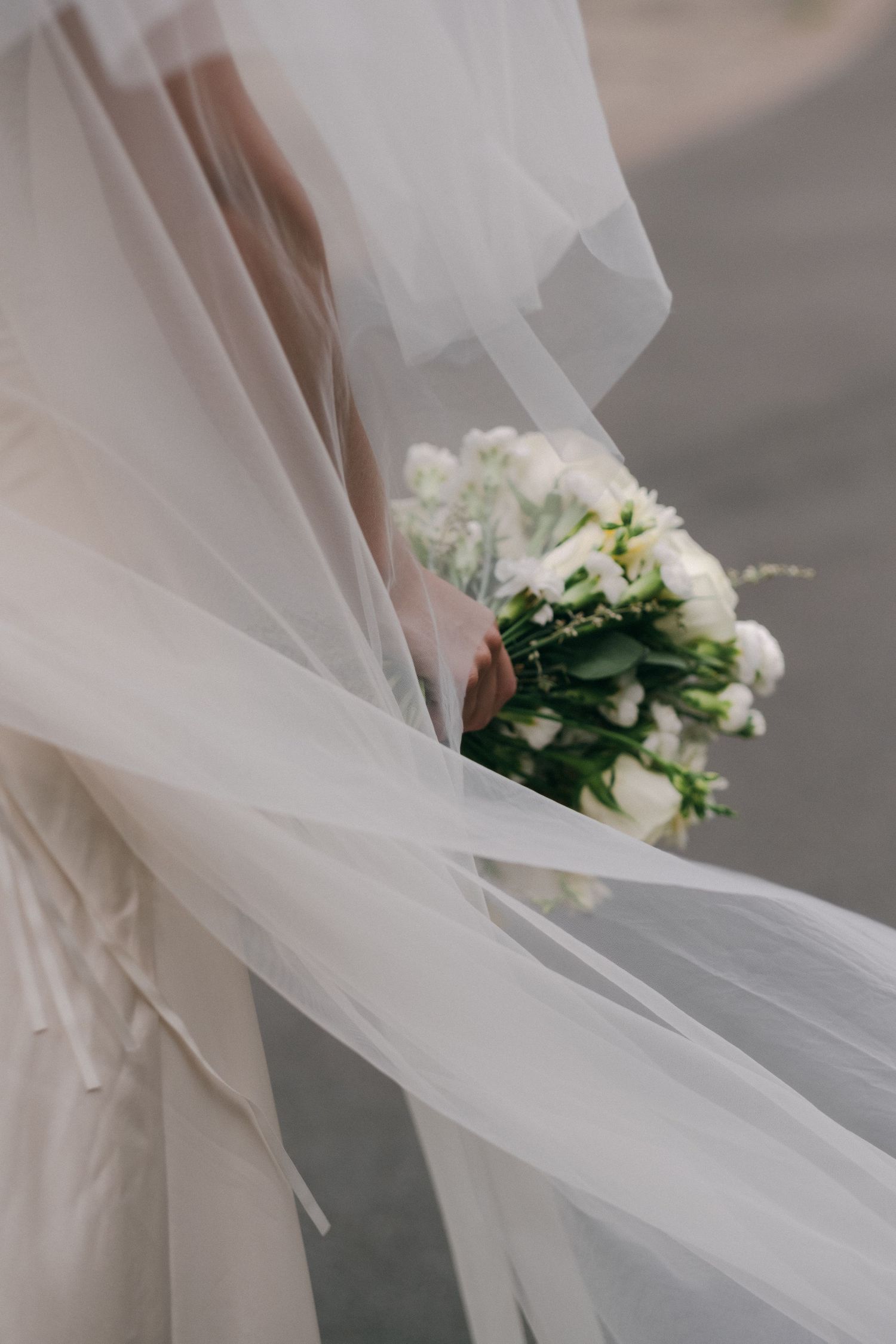 Close-up of a bride's flowing white veil and white rose wedding bouquet in the breeze.