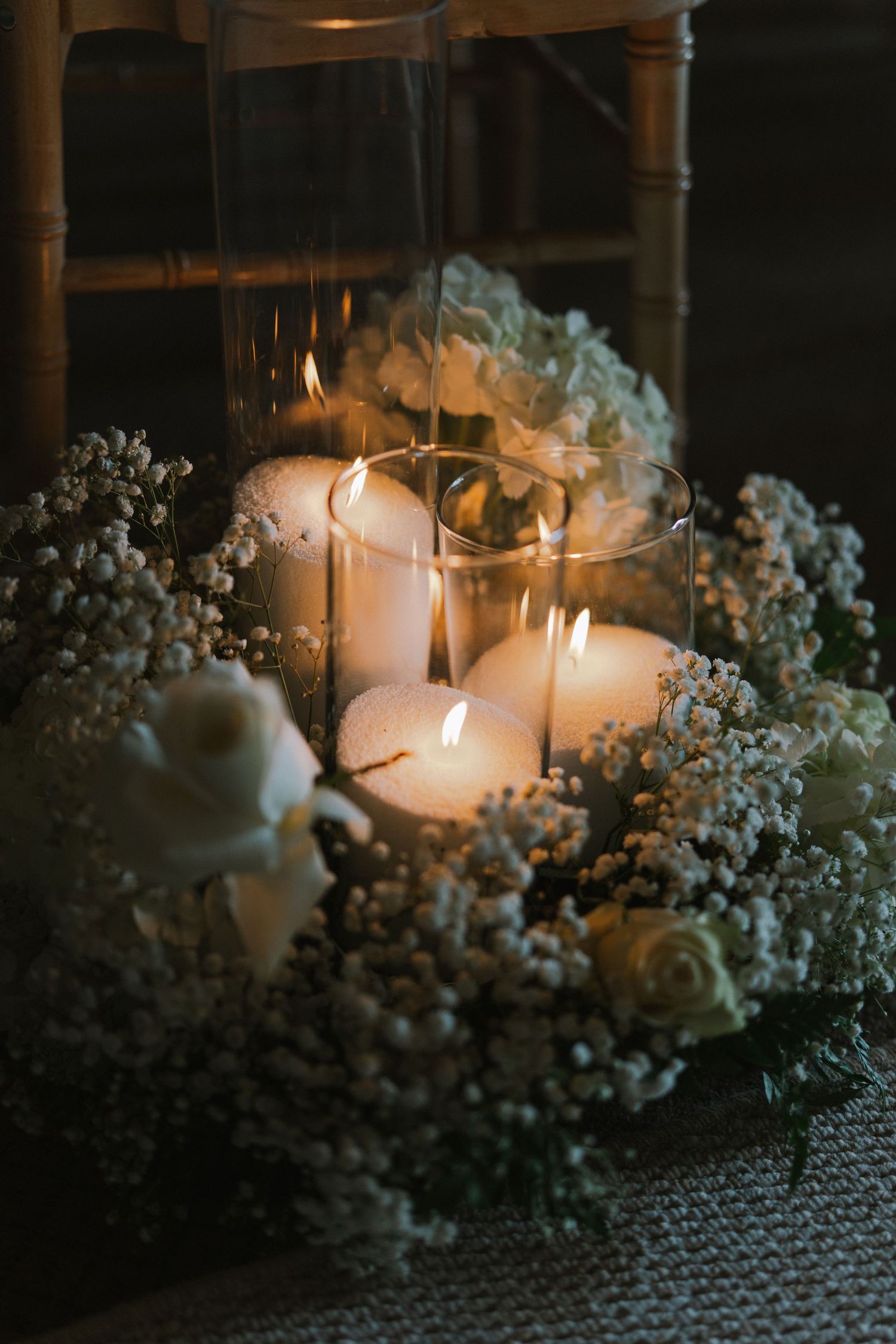 Elegant wedding centerpiece with lit pillar candles in glass vase surrounded by white roses and baby's breath flowers.