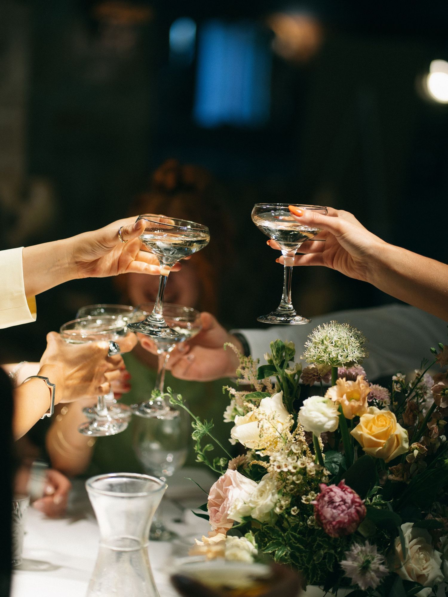 Guests clinking coupe glasses in a toast over a floral centerpiece at a wedding reception.