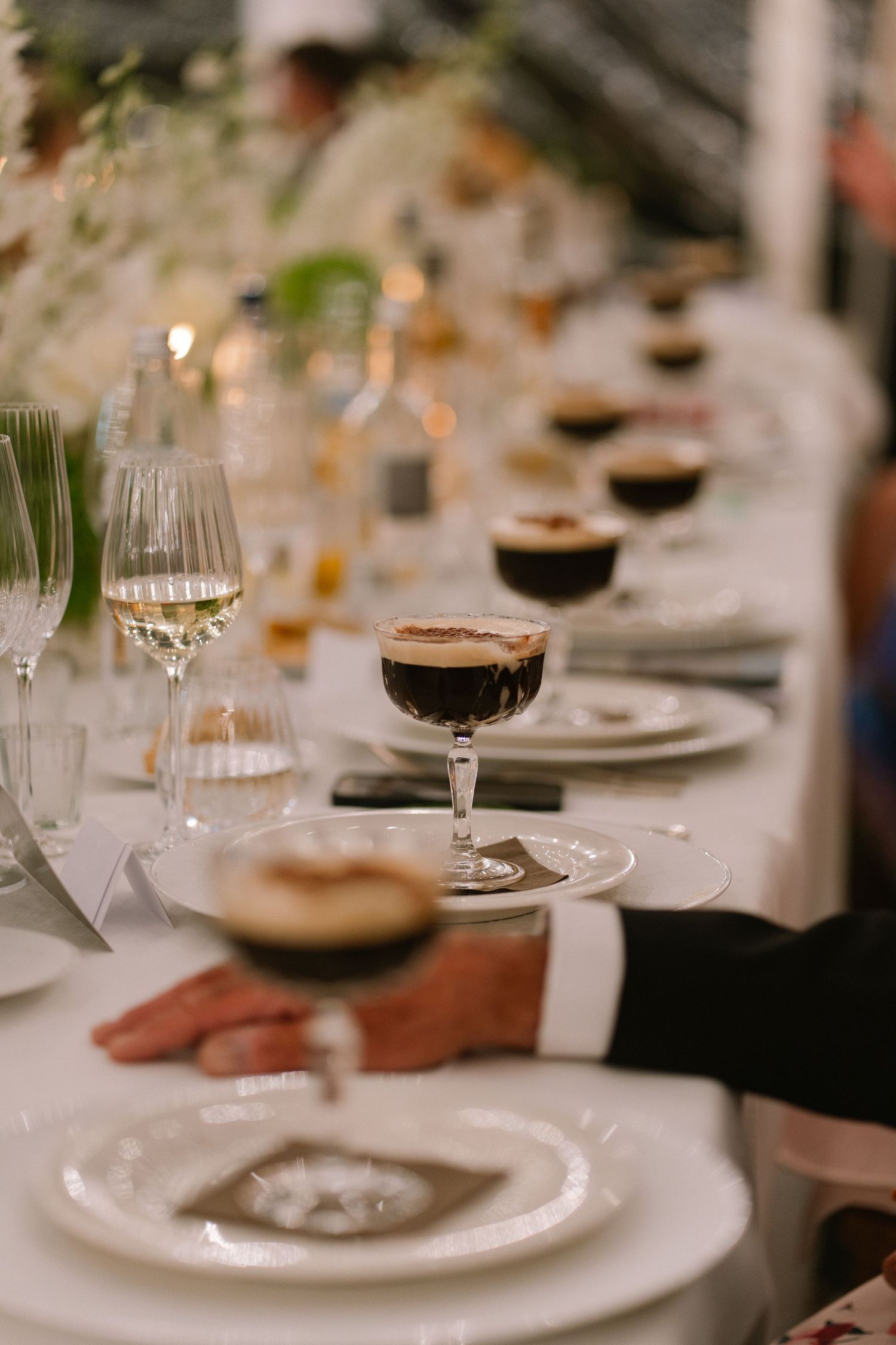 Elegant wedding reception table with espresso martinis in coupe glasses and white florals.