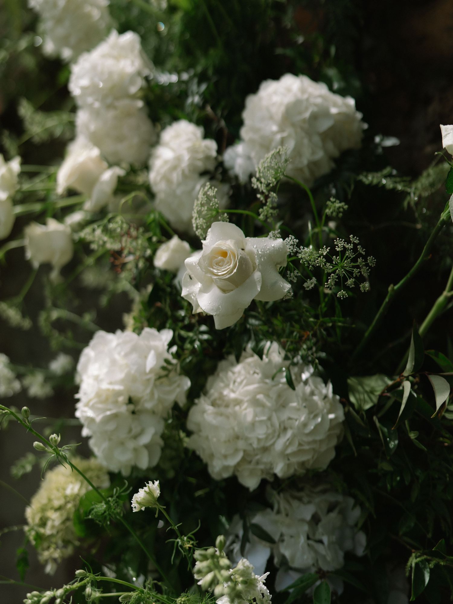 Elegant white floral arrangement with roses and hydrangeas for wedding ceremony decor.