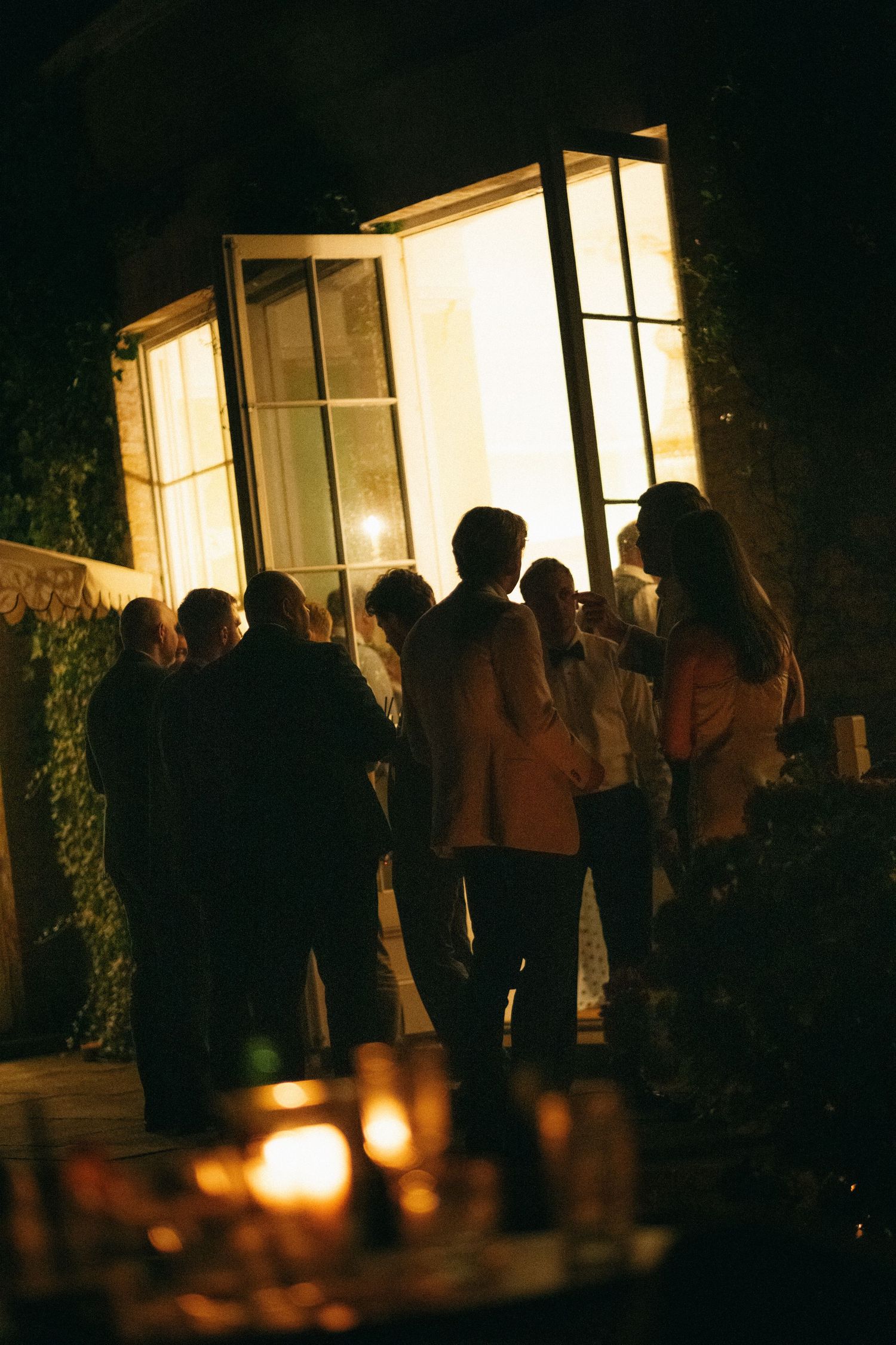 Guests silhouetted against glowing doorway at elegant evening outdoor gathering with candlelight ambiance.