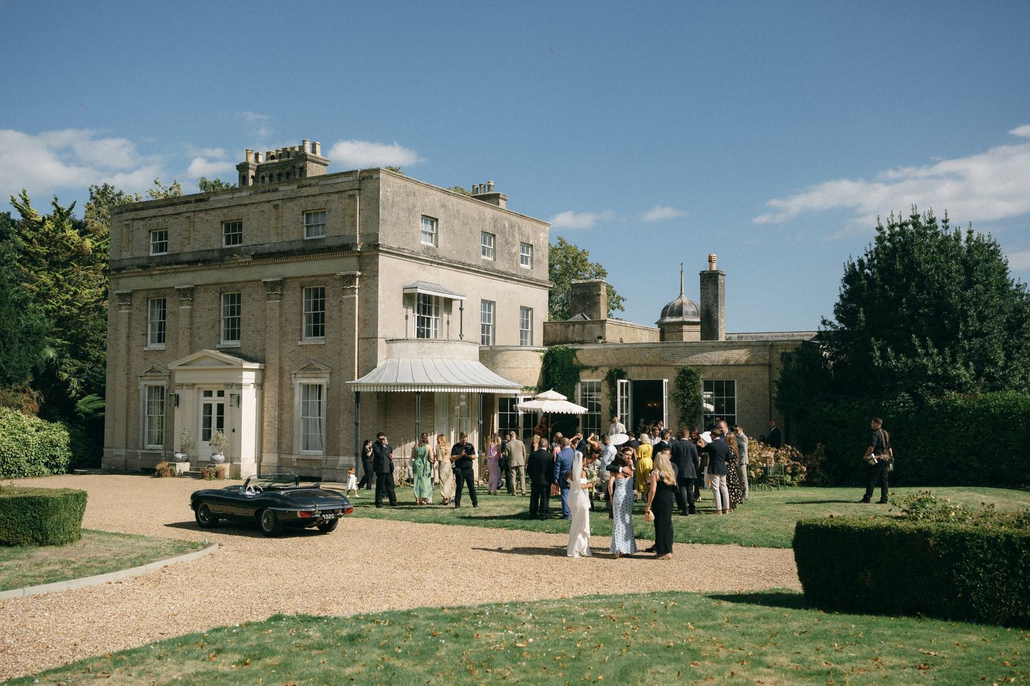 Elegant Georgian country house wedding venue with guests gathered outside on a sunny day.