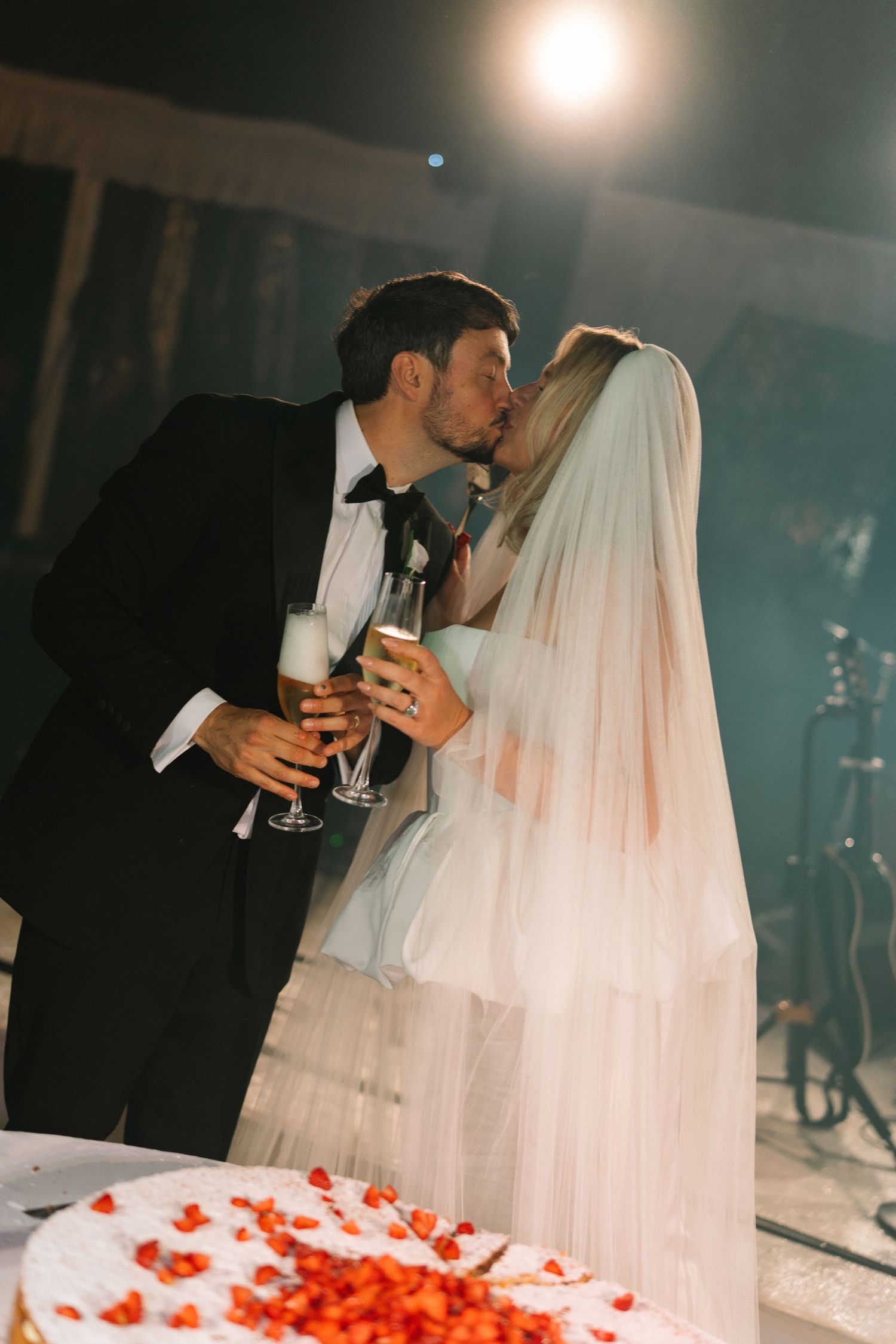 Bride and groom sharing a romantic kiss while holding champagne glasses at their wedding reception.