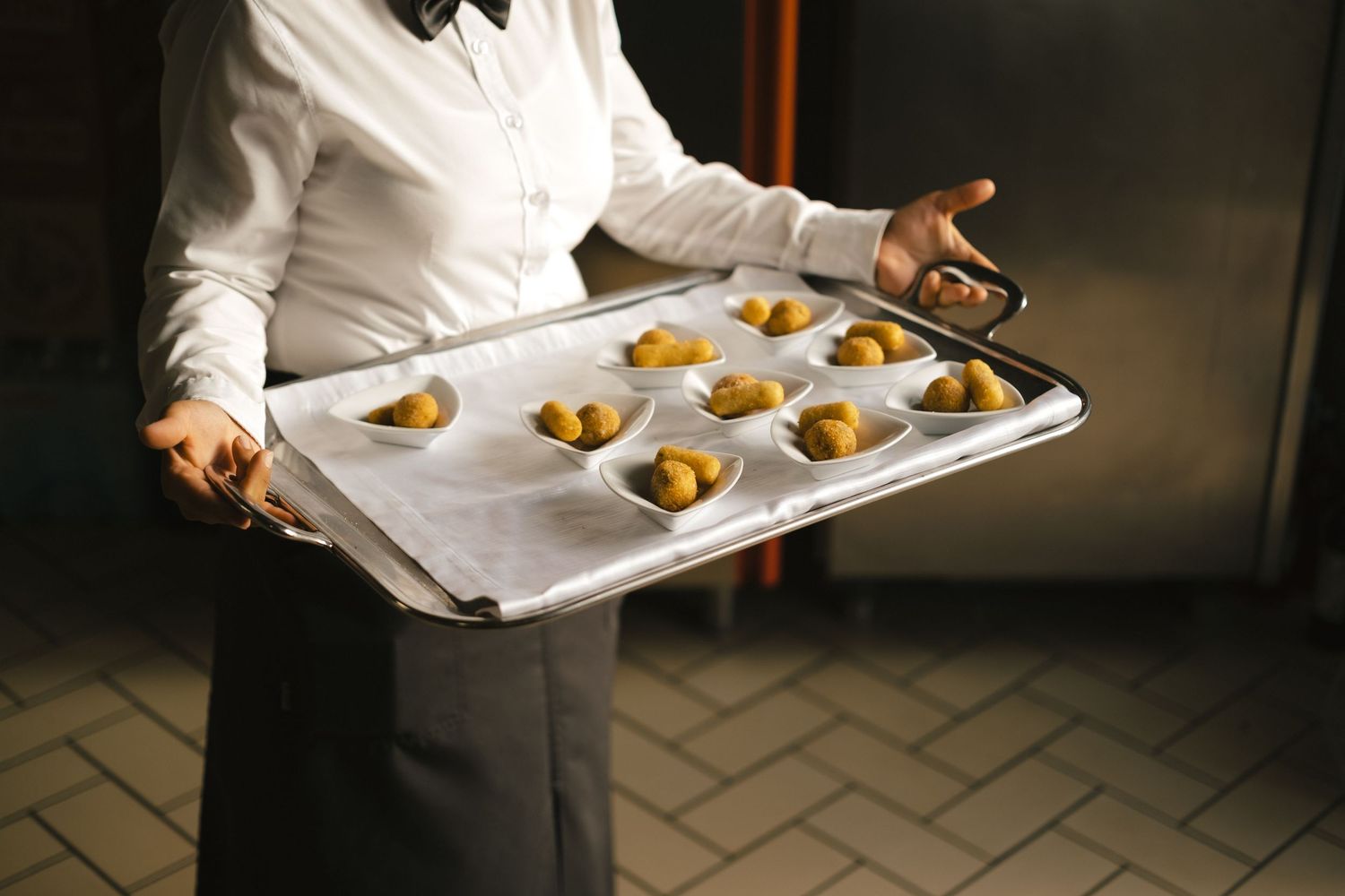 A server holding a baking tray with golden pastries on parchment paper in a professional kitchen.