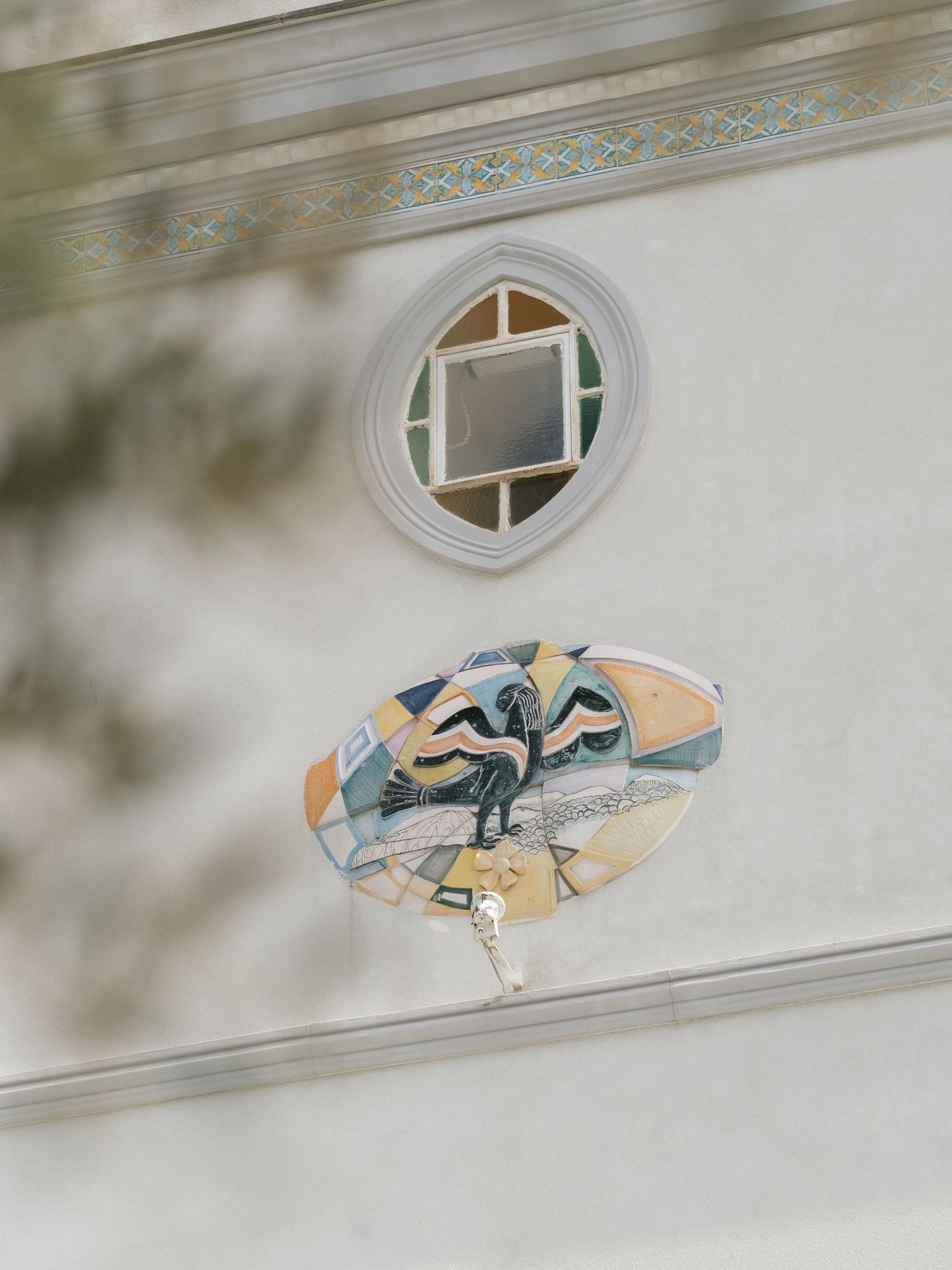 Decorative oval mosaic artwork and circular stained glass window on a white building facade with ornate border trim.