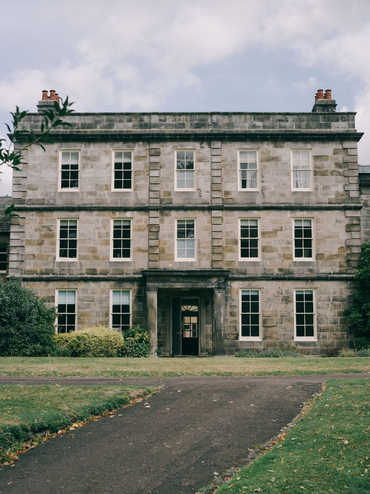 Historic Georgian stone manor house with symmetrical facade, large windows, and red chimneys set in manicured grounds.