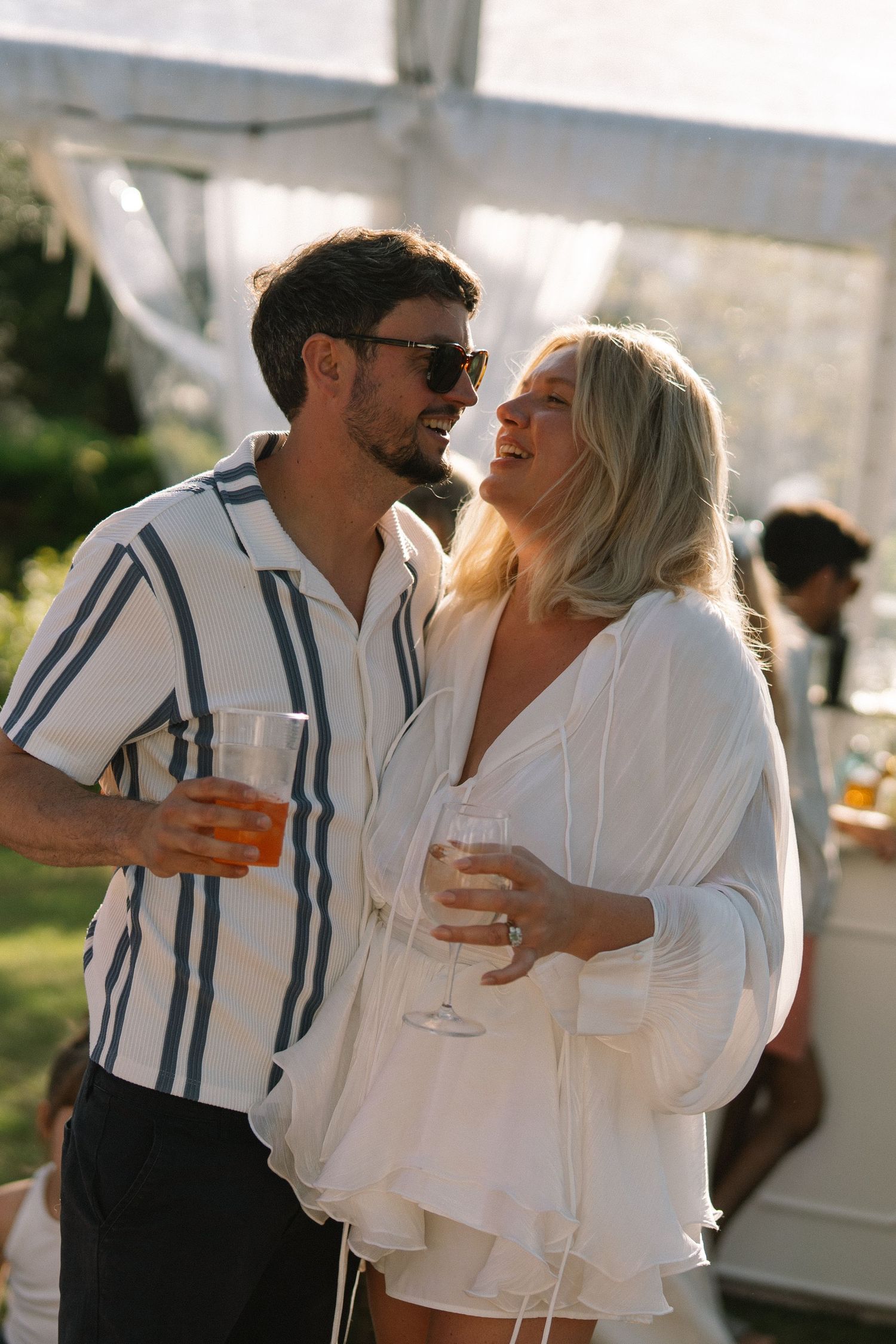 Couple sharing a romantic moment at an outdoor party, holding champagne glasses in sunny garden setting.