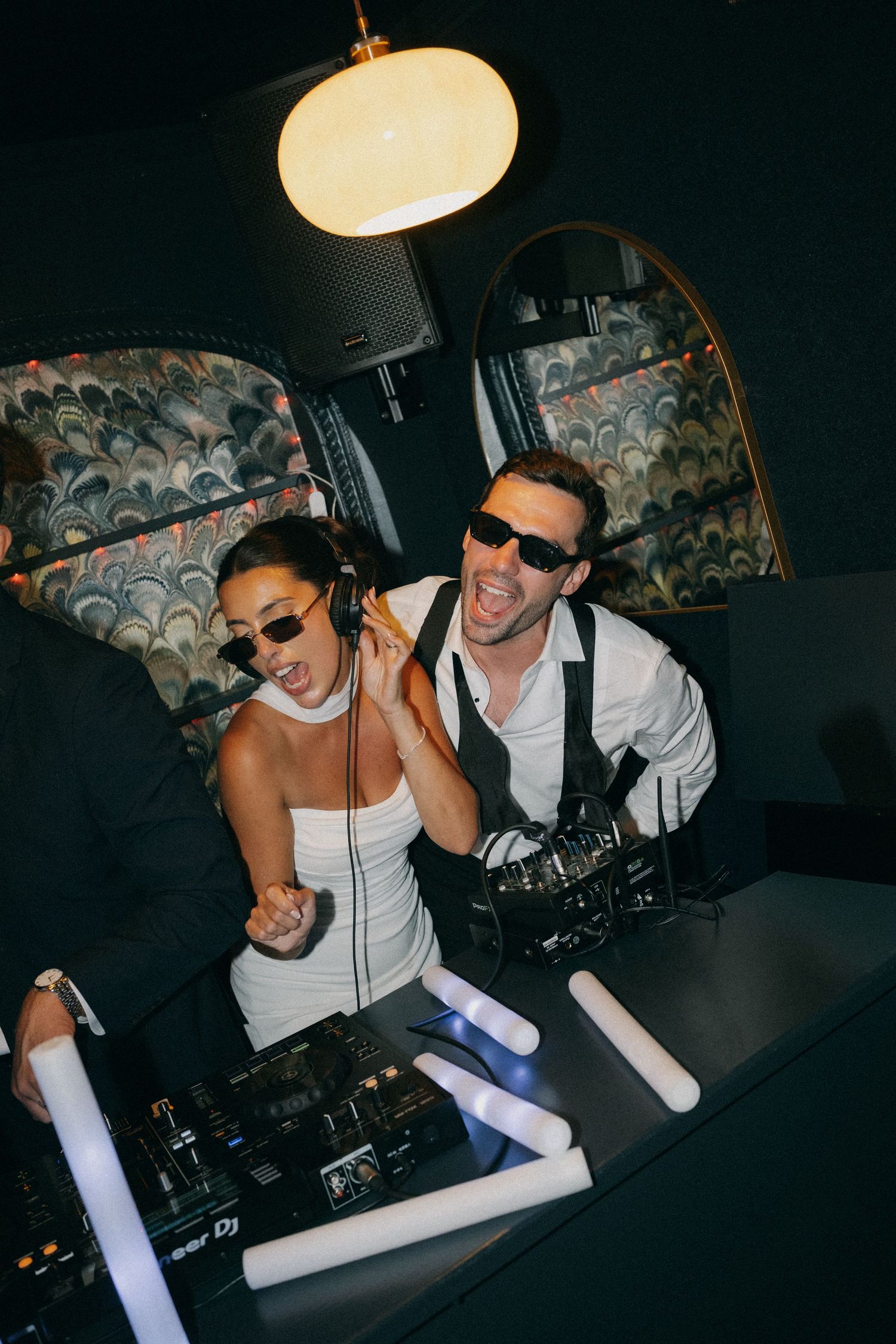 Bride and groom DJing together at wedding reception, wearing sunglasses and dancing behind Pioneer DJ decks.
